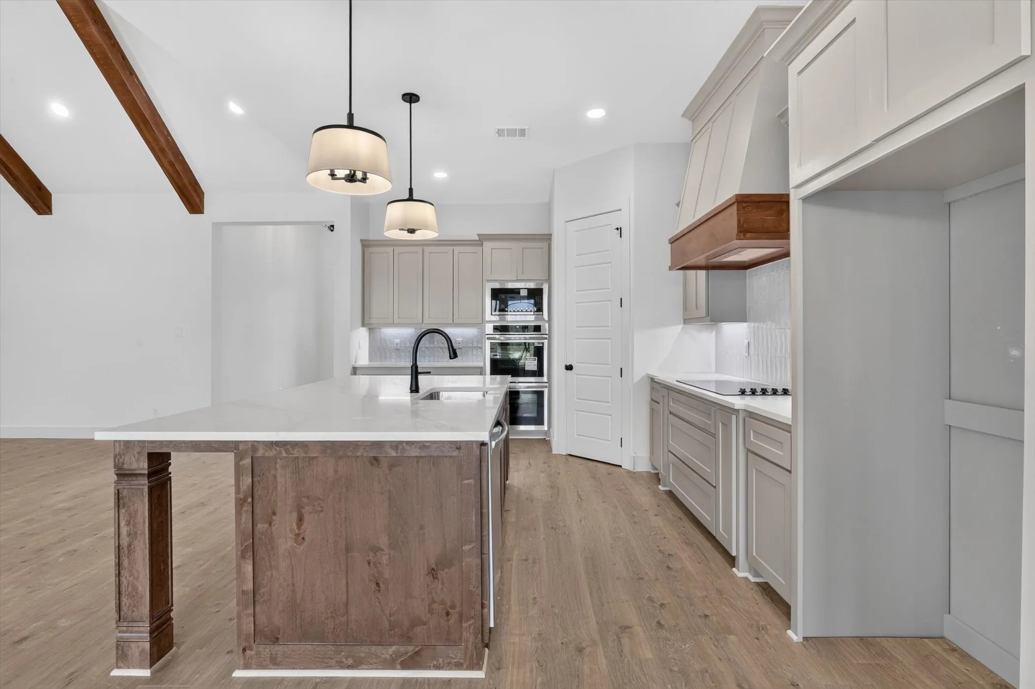 Kitchen featuring a large island with a white countertop and dark wood-finish cabinetry, light grey perimeter cabinetry, and built-in double ovens