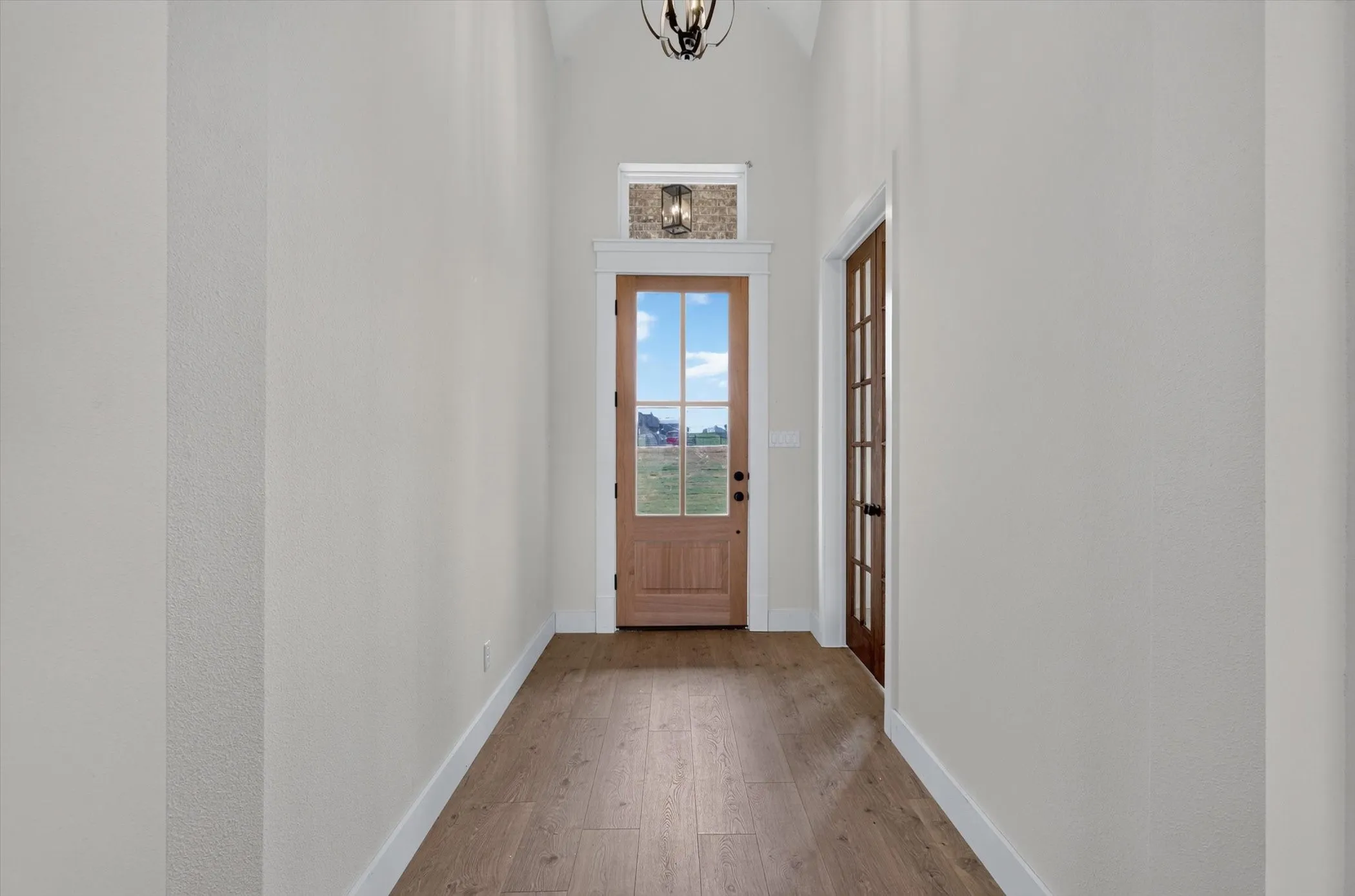Entryway featuring vaulted ceilings, wood-finish flooring, and a natural wood front door with glass panels