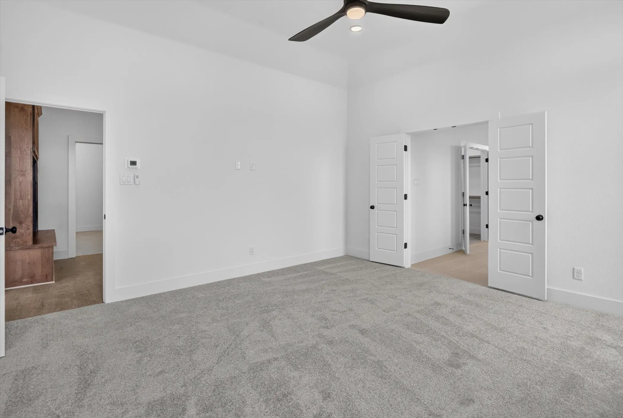 Spacious room featuring vaulted ceilings, light gray carpet flooring, a ceiling fan with integrated lighting, and white baseboards