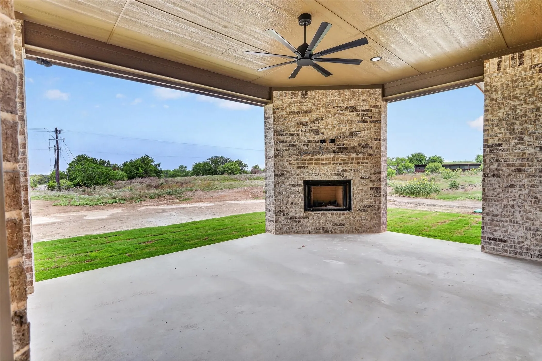 Covered outdoor patio featuring a brick fireplace with an integrated firebox, a ceiling fan, recessed lighting, and a concrete floor