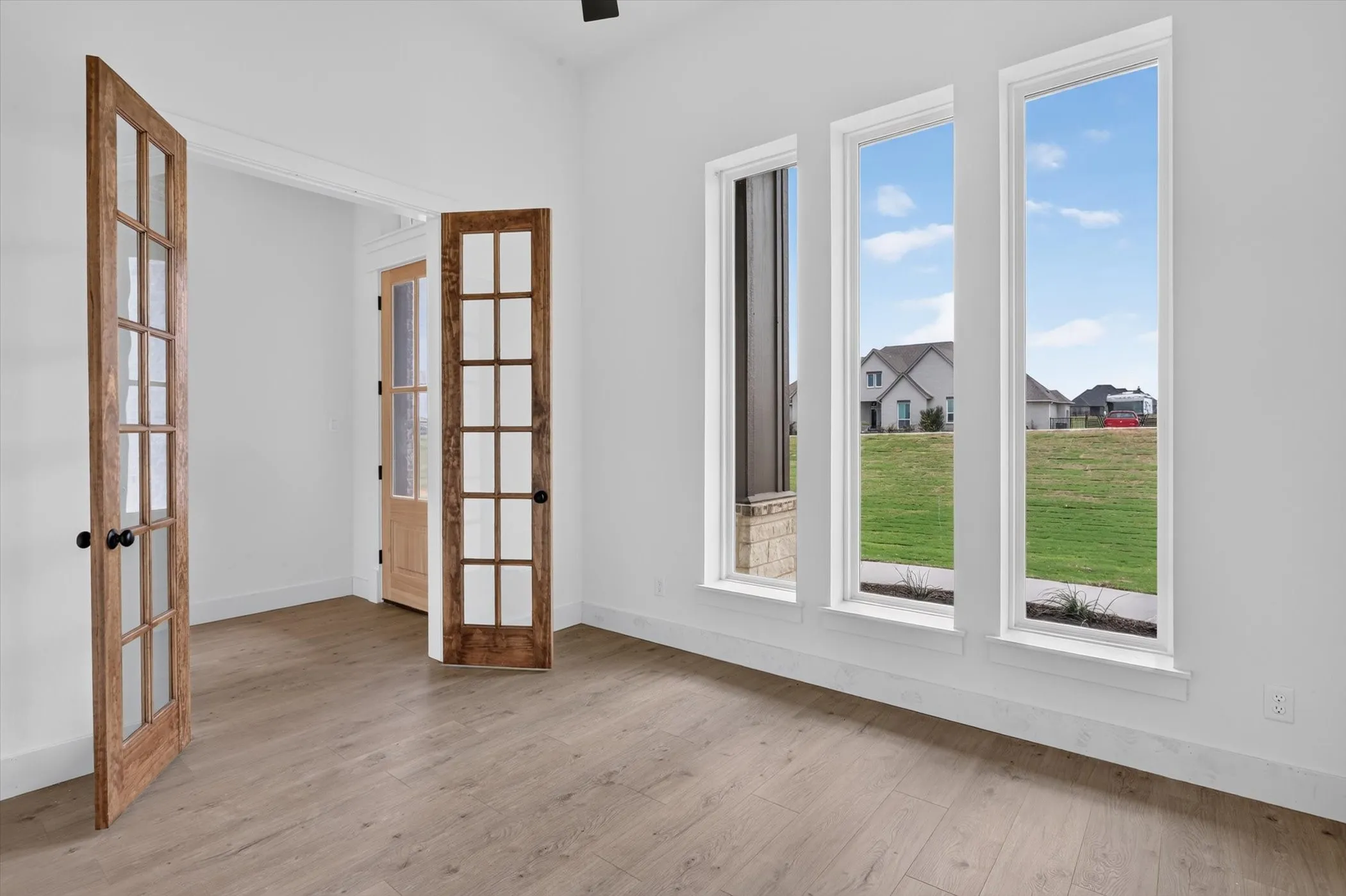 Room featuring three tall windows, light wood-finish flooring, white baseboards, and double French doors with black hardware