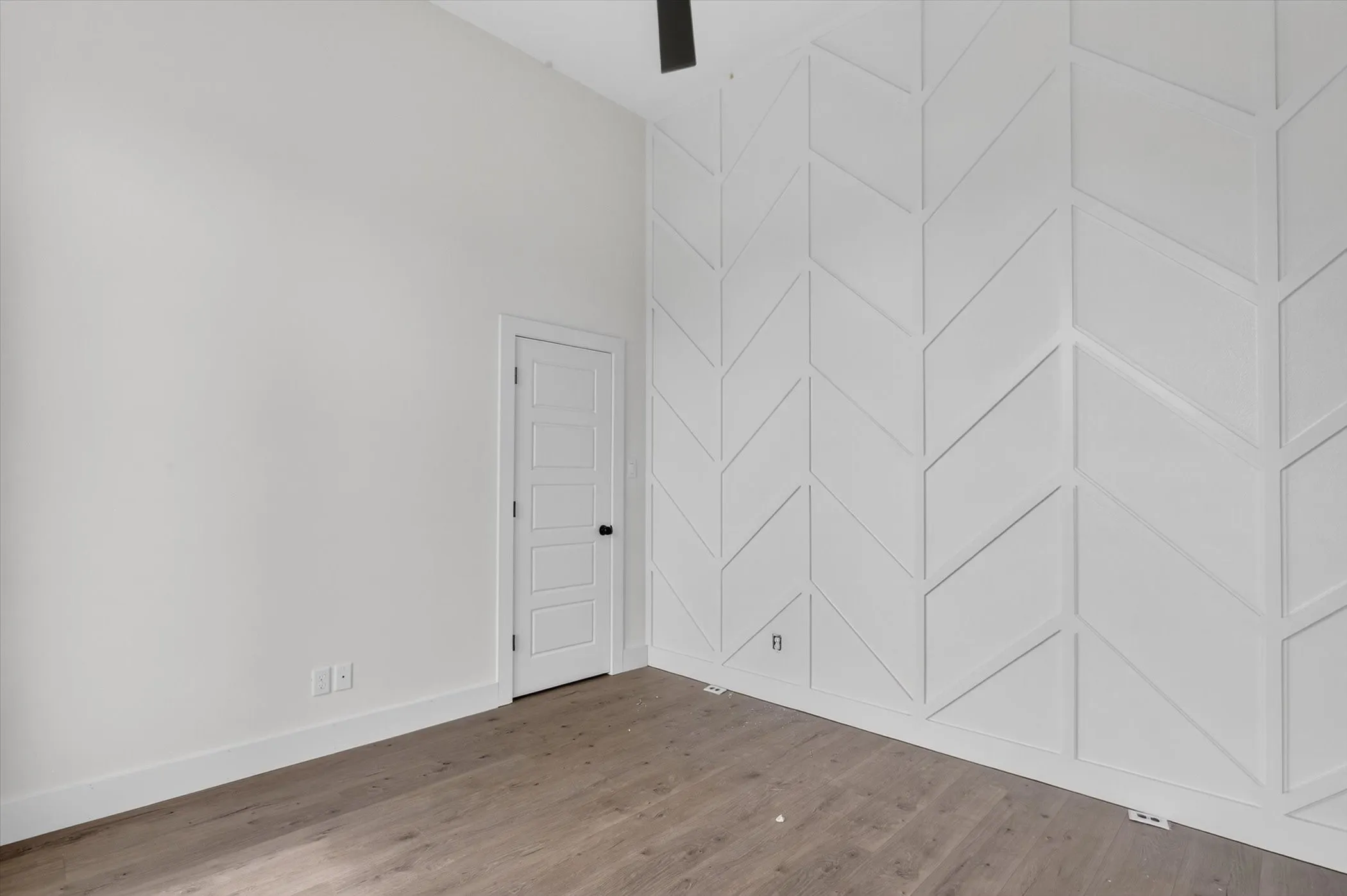 Vaulted ceiling room featuring a decorative accent wall with a geometric pattern, wood-finish flooring, and a paneled interior door with black​​‌​​​​‌​​‌‌​‌‌​​​‌‌​‌​‌​‌​​​‌​​ hardware