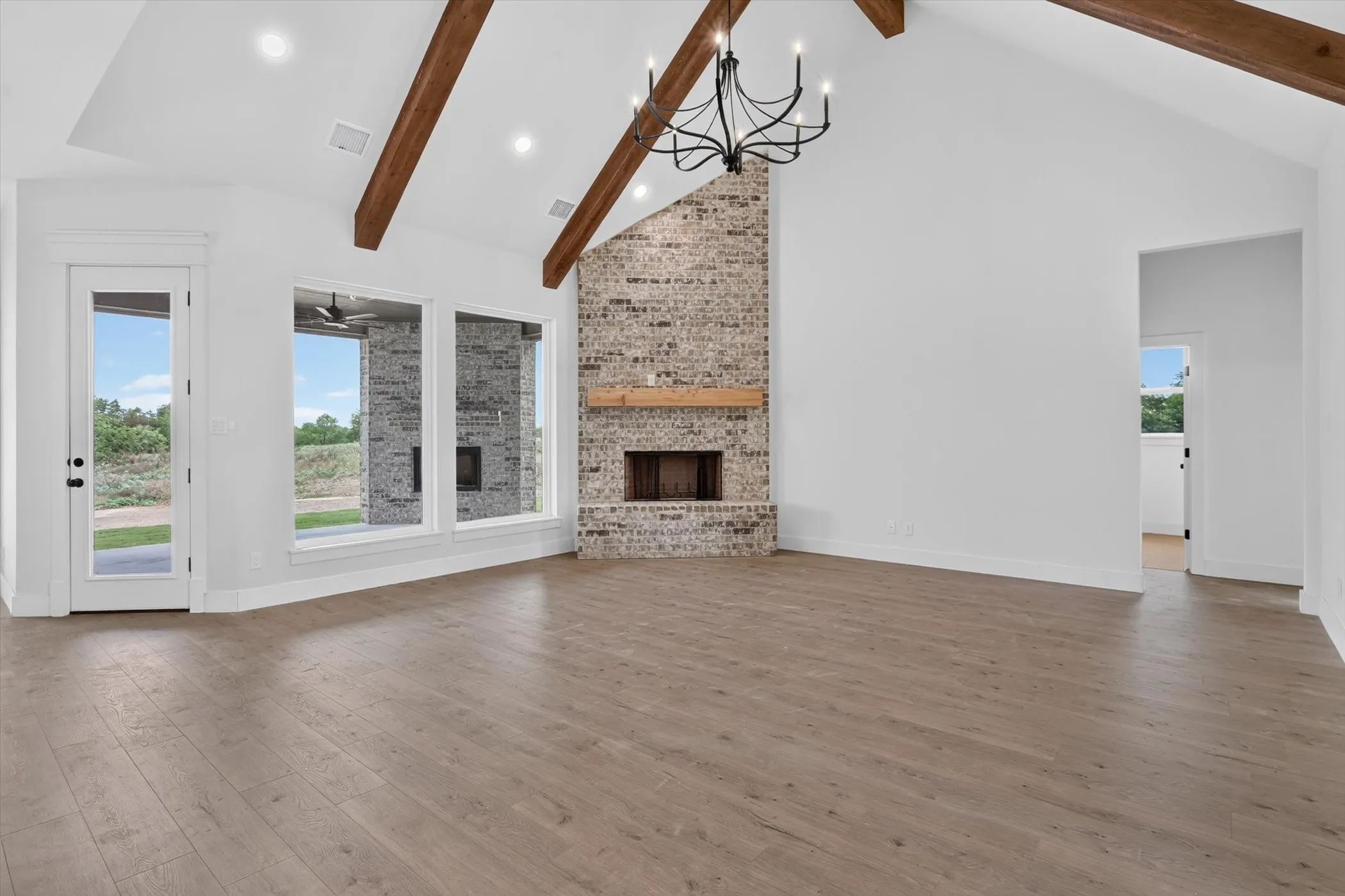 Spacious room featuring vaulted ceilings with exposed wood beams, a brick fireplace with a wood mantle, and wood-finish flooring