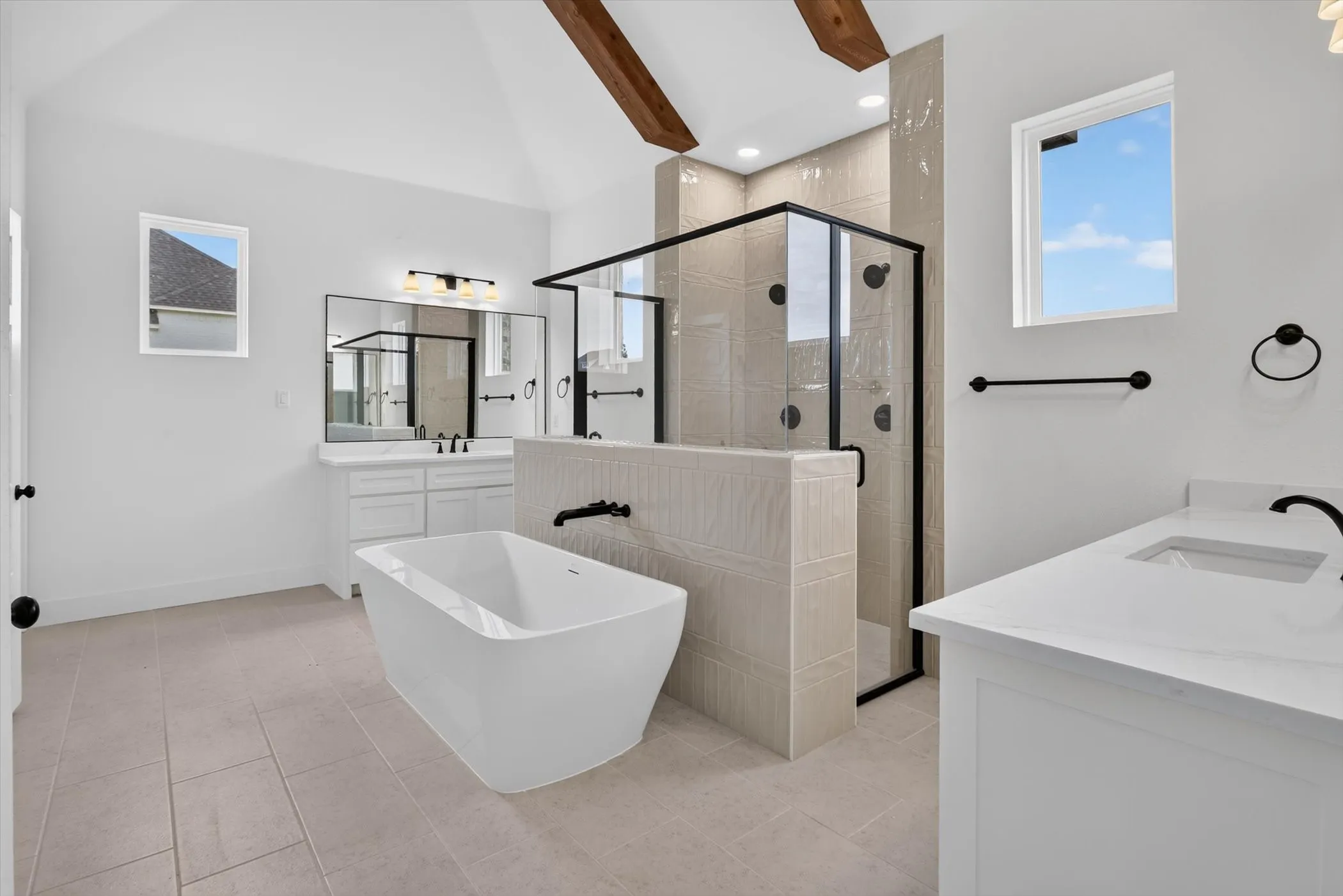 Spacious bathroom featuring a freestanding soaking tub, a large walk-in shower with black-framed glass enclosure, and dual vanity areas with white cabinetry and solid surface countertops