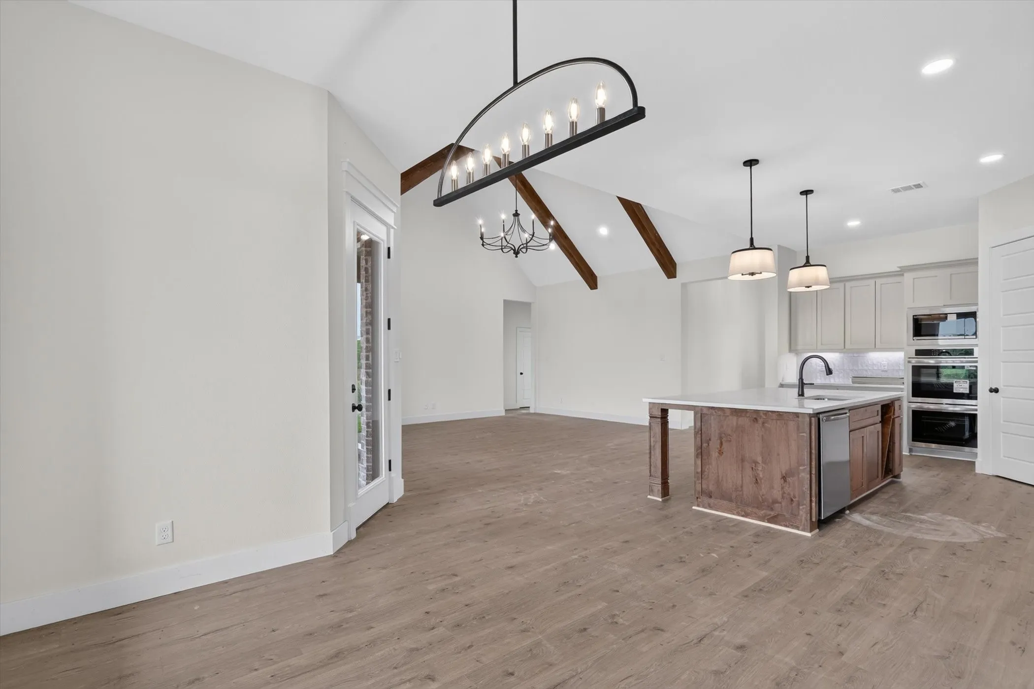 Open-concept living space featuring wood-finish flooring, vaulted ceilings with exposed beams, and contemporary lighting