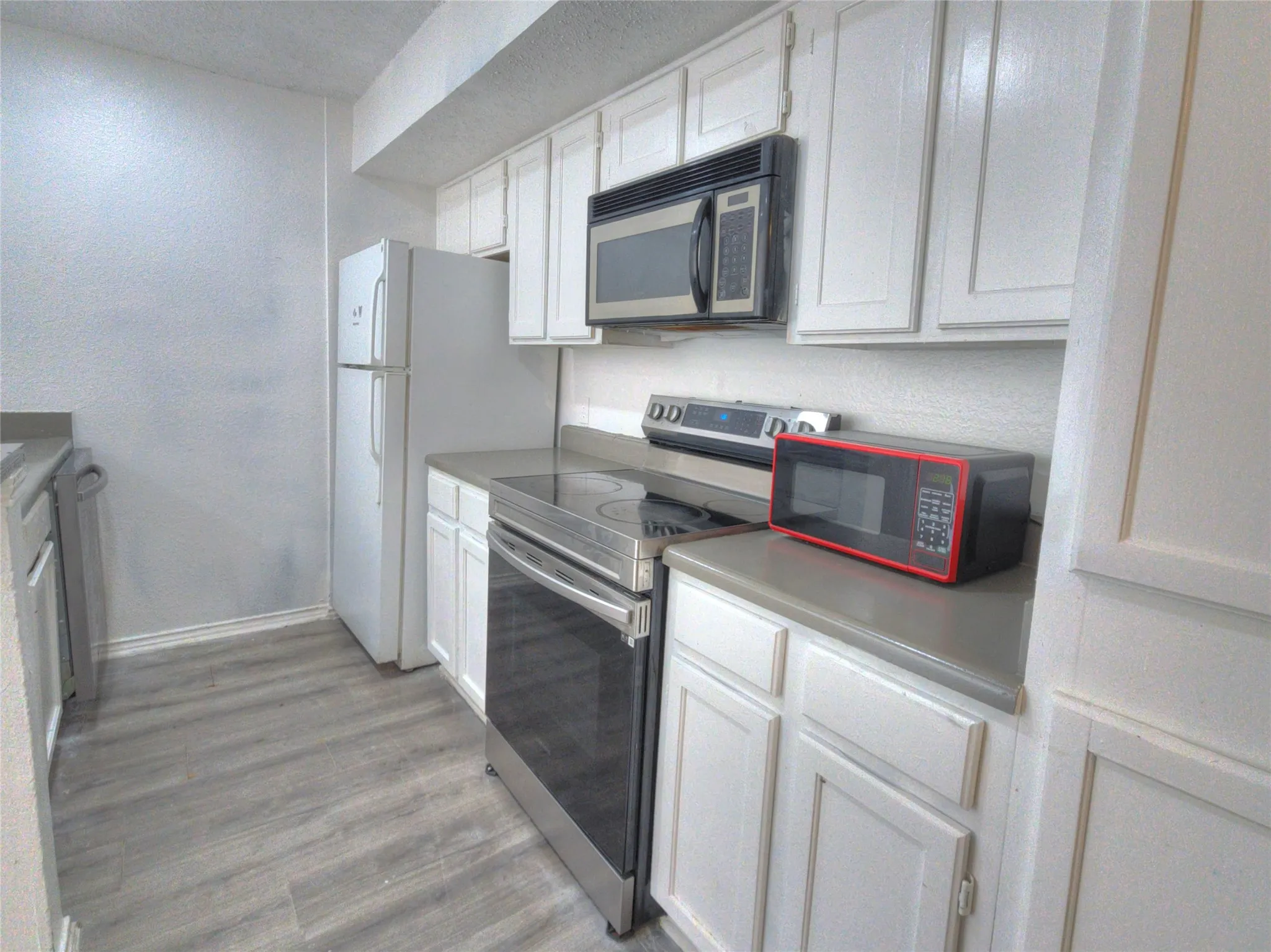 Kitchen with wood-finish flooring, white cabinetry, a built-in microwave, and stainless steel range