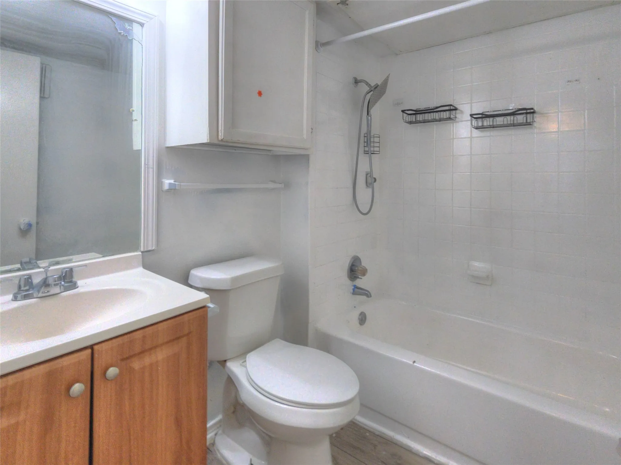 Wood-finish vanity with an integrated sink, polished chrome faucet, white tile shower surround, and a built-in bathtub