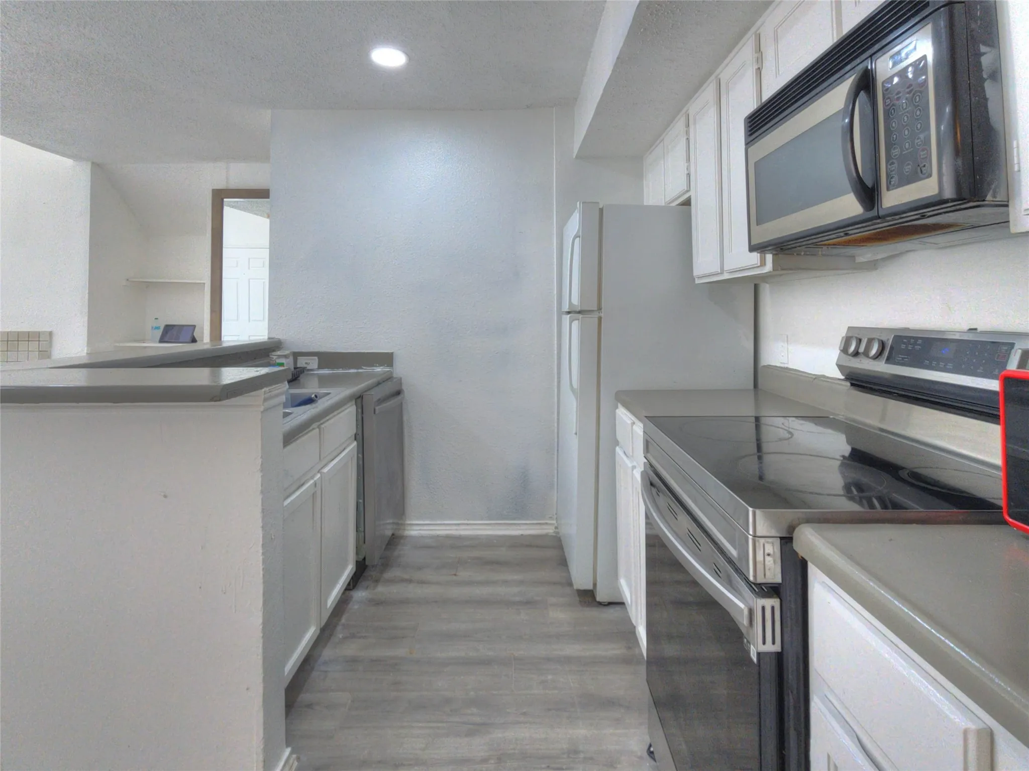 Galley kitchen with wood-finish flooring, white cabinetry, and gray countertops