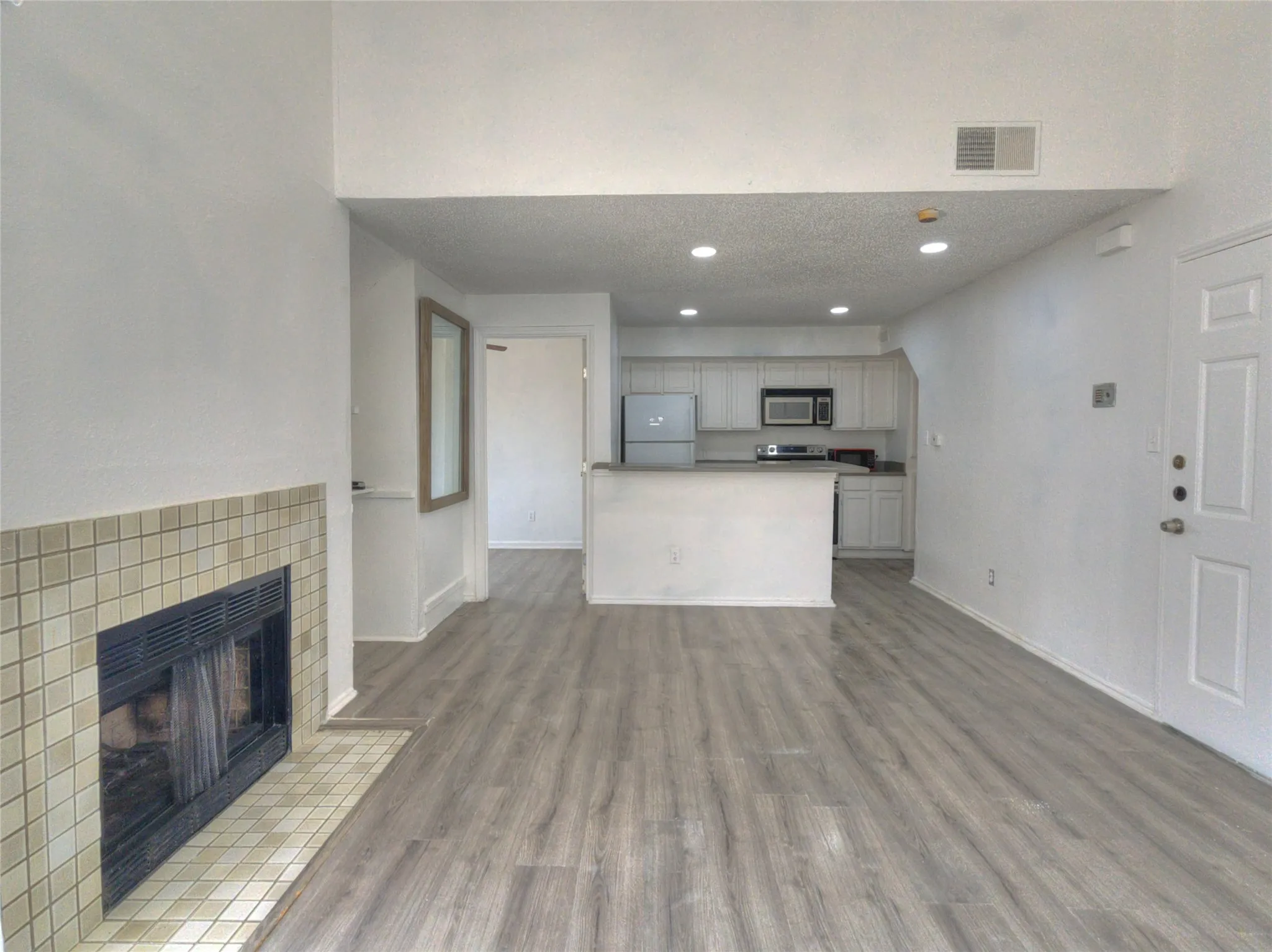 Open concept living area with wood-finish flooring, a tiled fireplace, and recessed lighting
