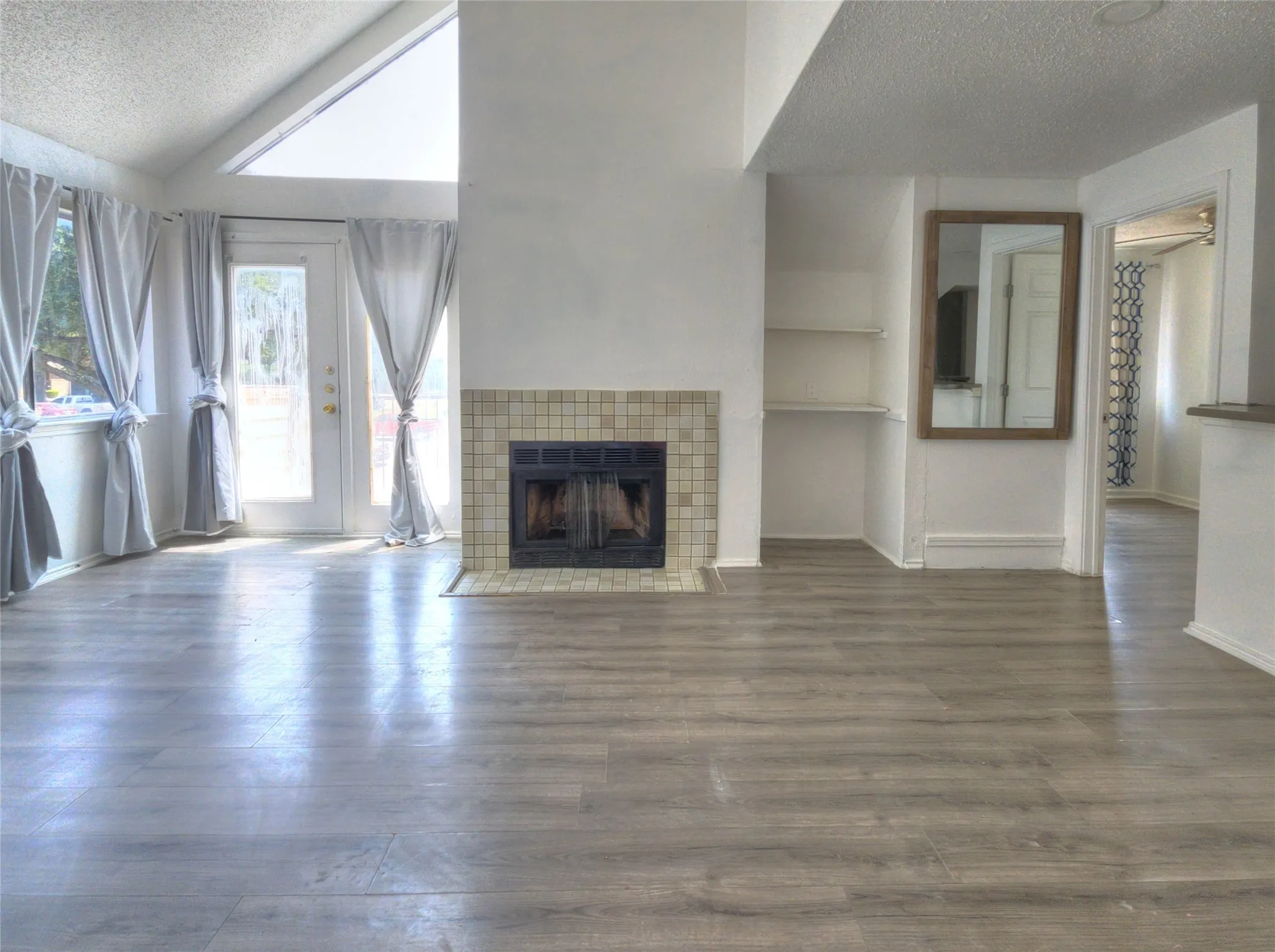 Vaulted ceiling with an architectural window, wood-finish flooring, tiled fireplace, and built-in shelving