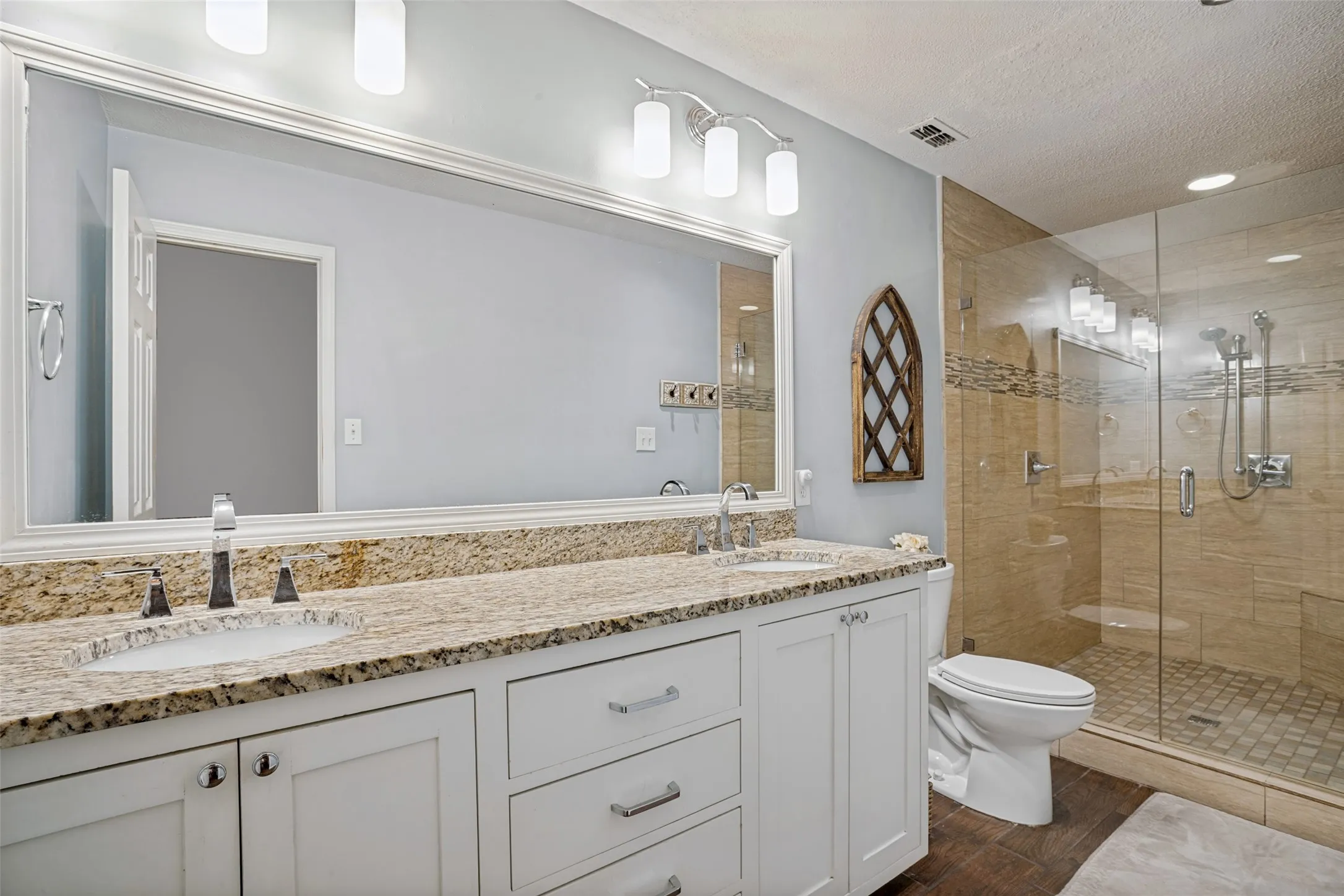 The spa-like primary bathroom has been beautifully remodeled with a granite vanity, an expansive frameless glass shower, a framed mirror, updated lighting, and a new toilet.