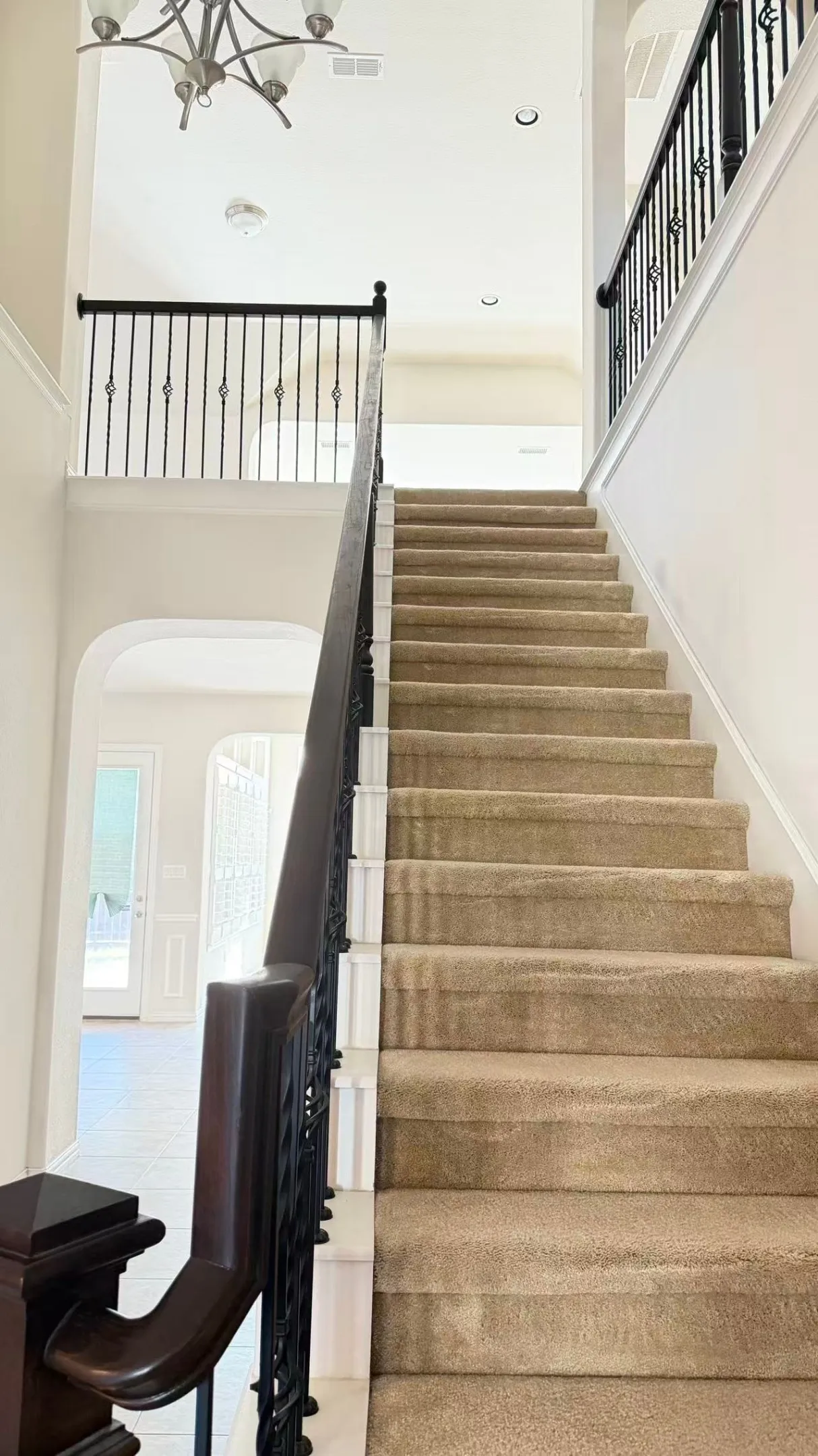 Two-story entry with a chandelier, carpeted staircase, dark wood handrail, and wrought iron balusters