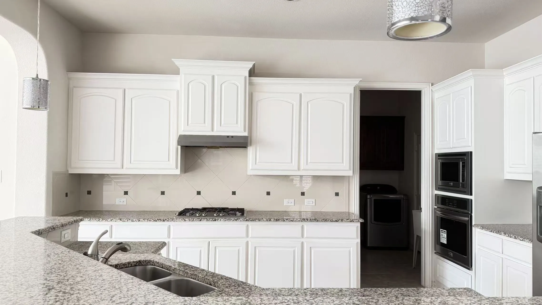 White cabinetry with crown molding, granite countertops, tile backsplash, built-in double oven, and gas cooktop