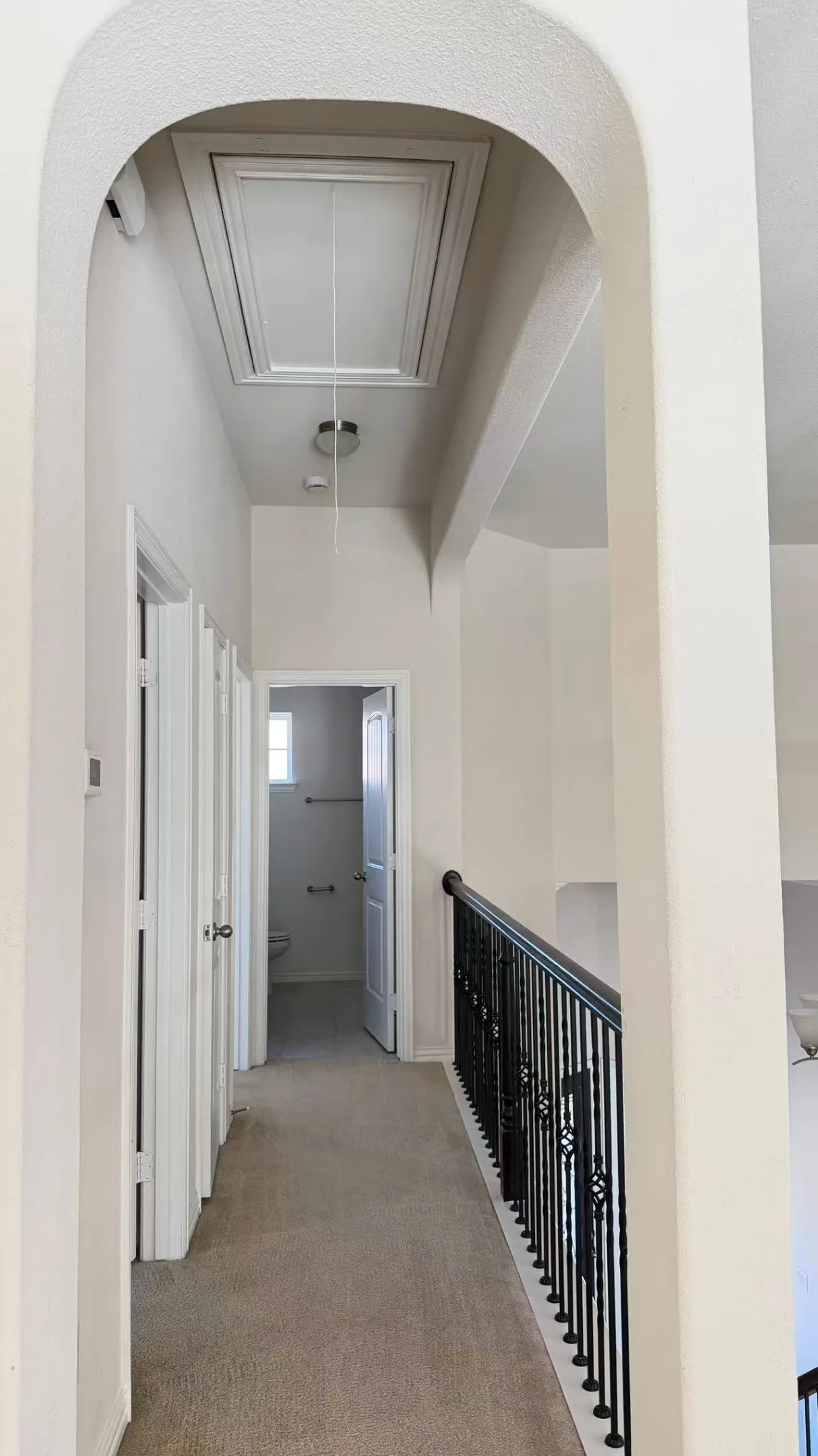 Arched entryway leading to a carpeted hallway with a pull-down attic access