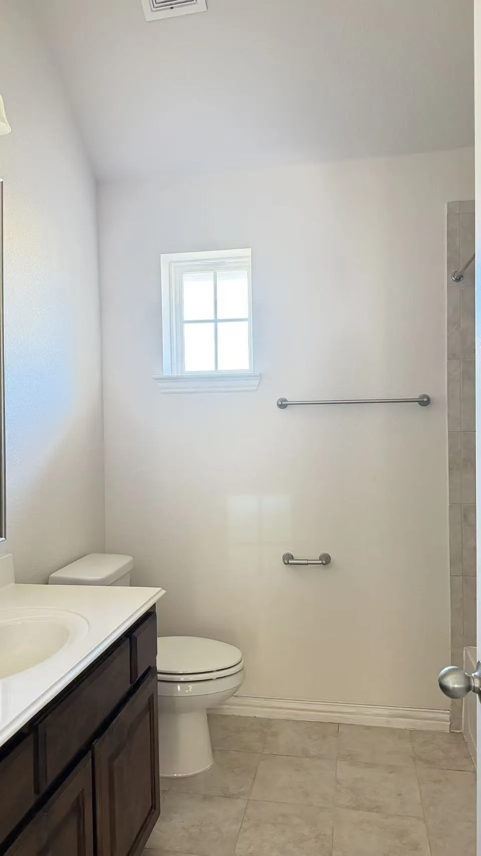 White bathroom featuring a window, vanity with wood-finish cabinetry, and tiled flooring