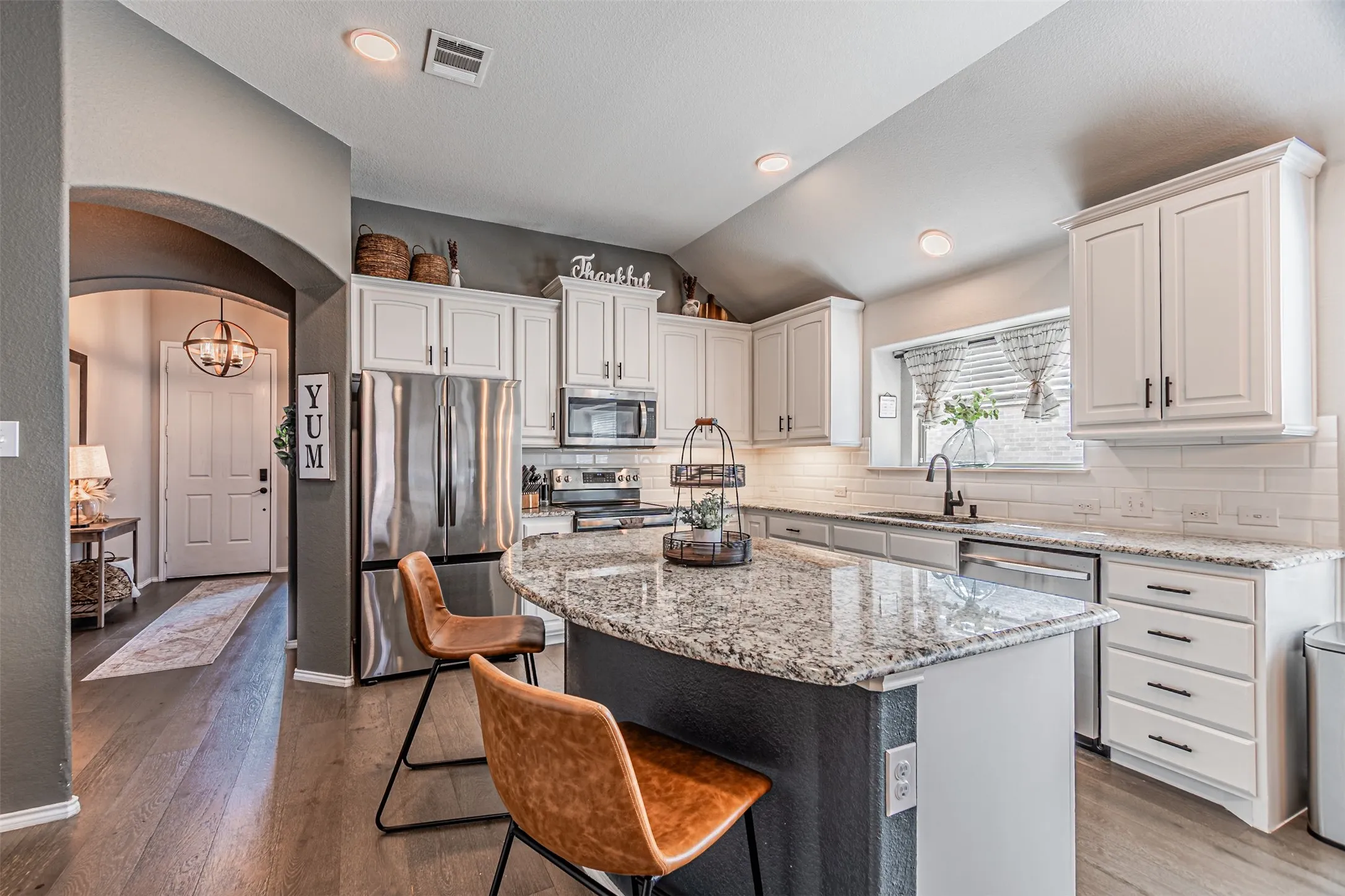 Kitchen with arched walkways, stainless steel appliances, light stone countertops, a breakfast bar area, and dark wood-style floors