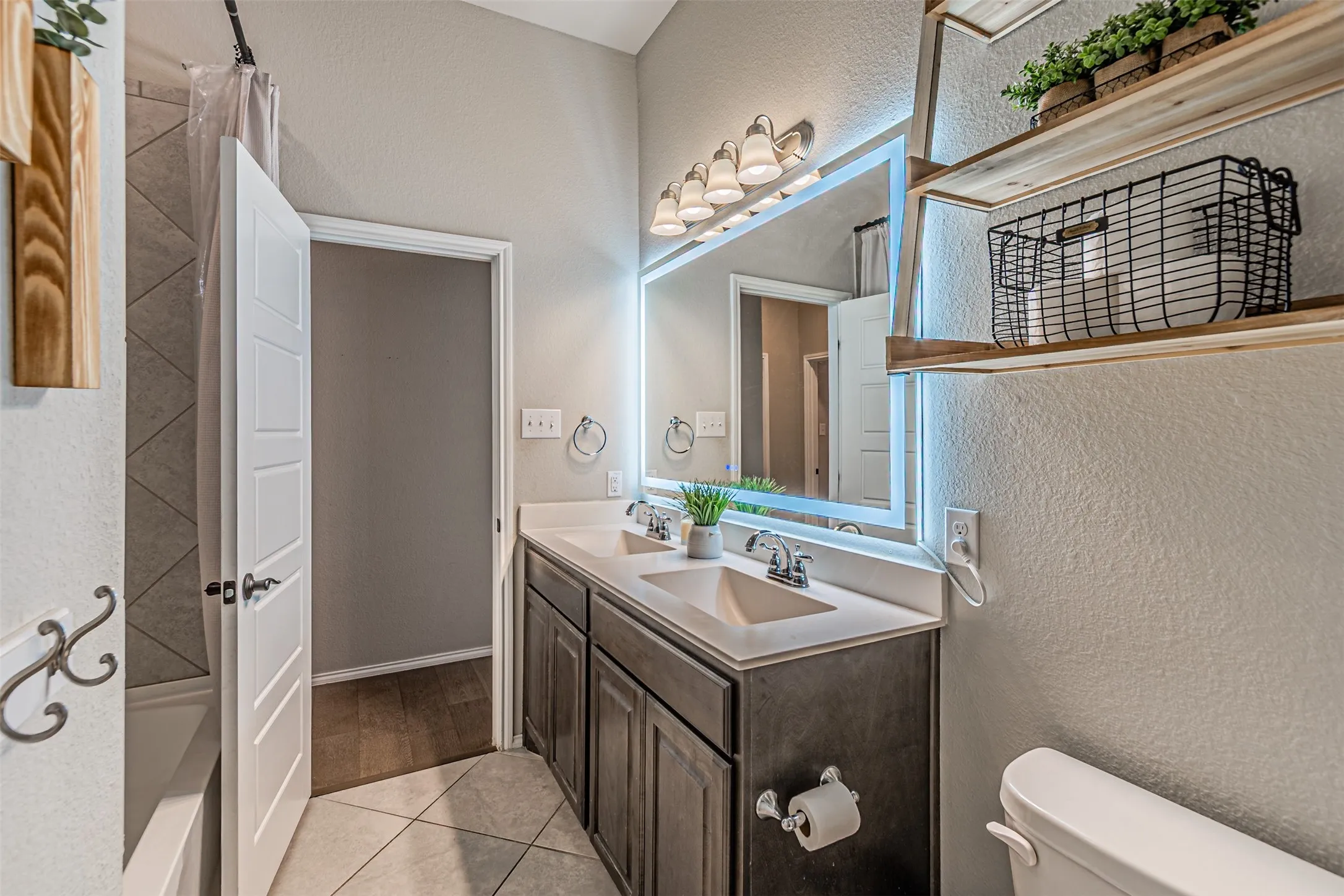 Bathroom with a textured wall, double vanity, and light tile patterned floors