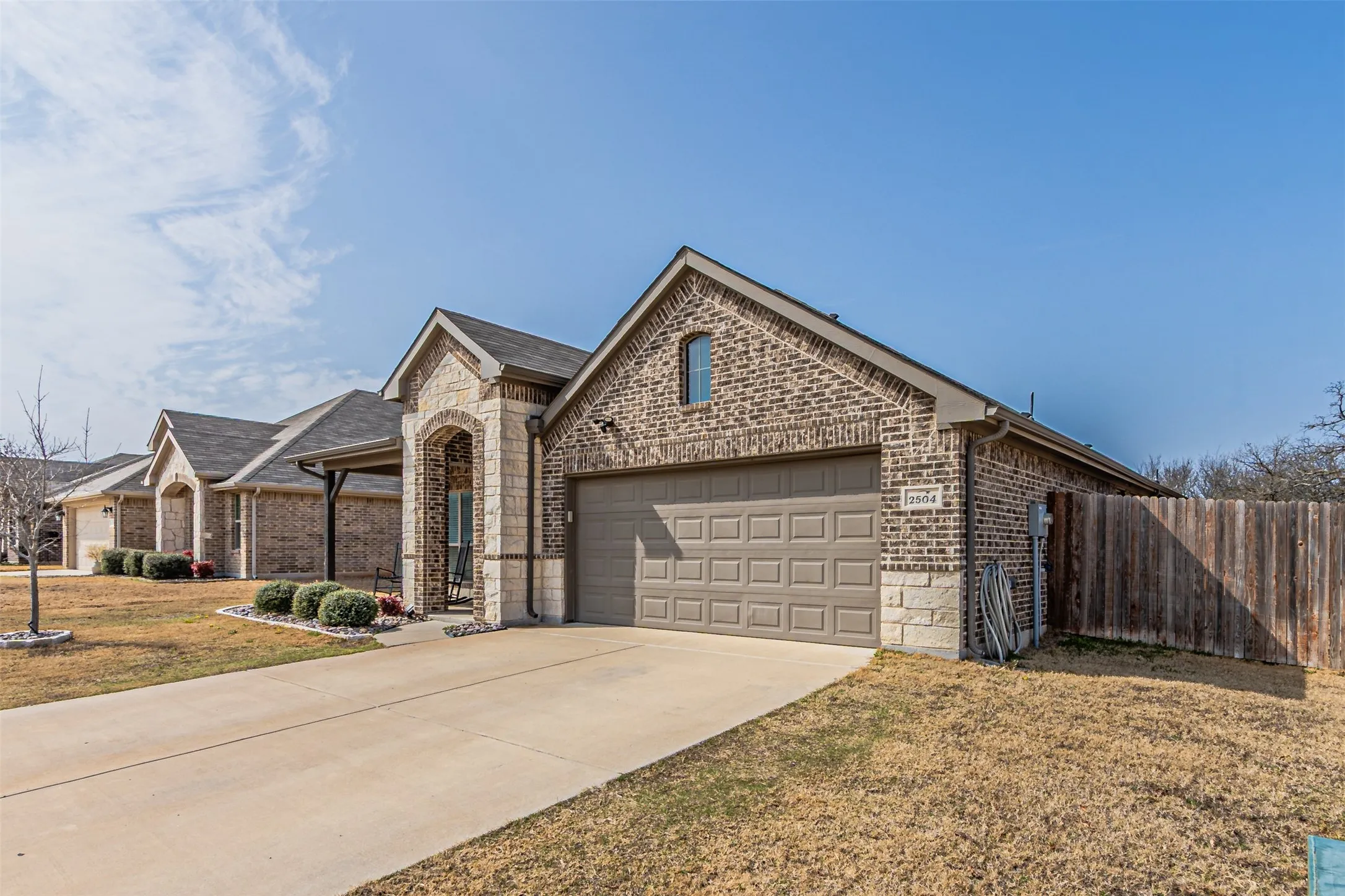 View of front of house with brick siding, driveway, an attached garage, stone siding, and a porch