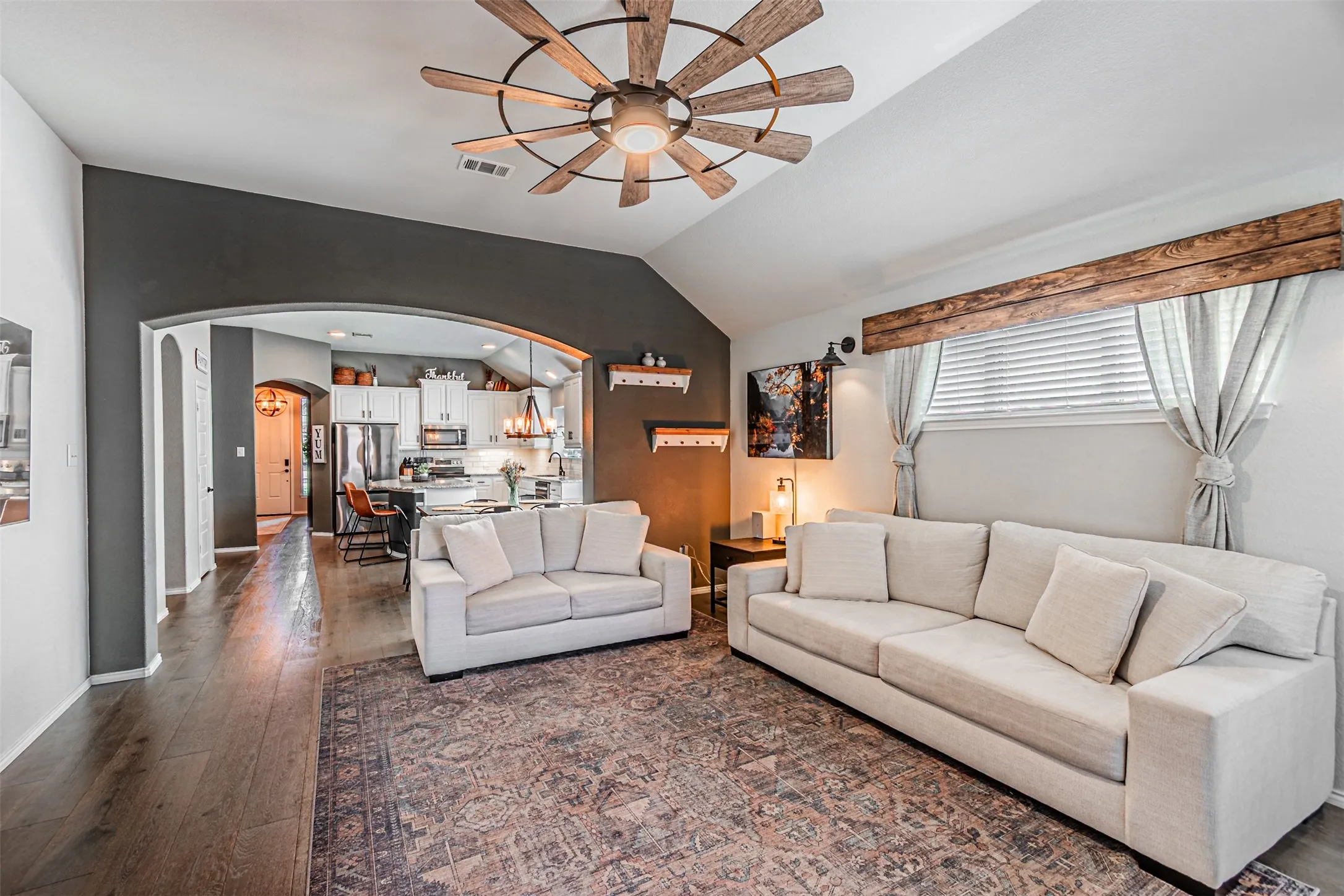 Living area featuring ceiling fan, arched walkways, dark wood-style floors, and lofted ceiling