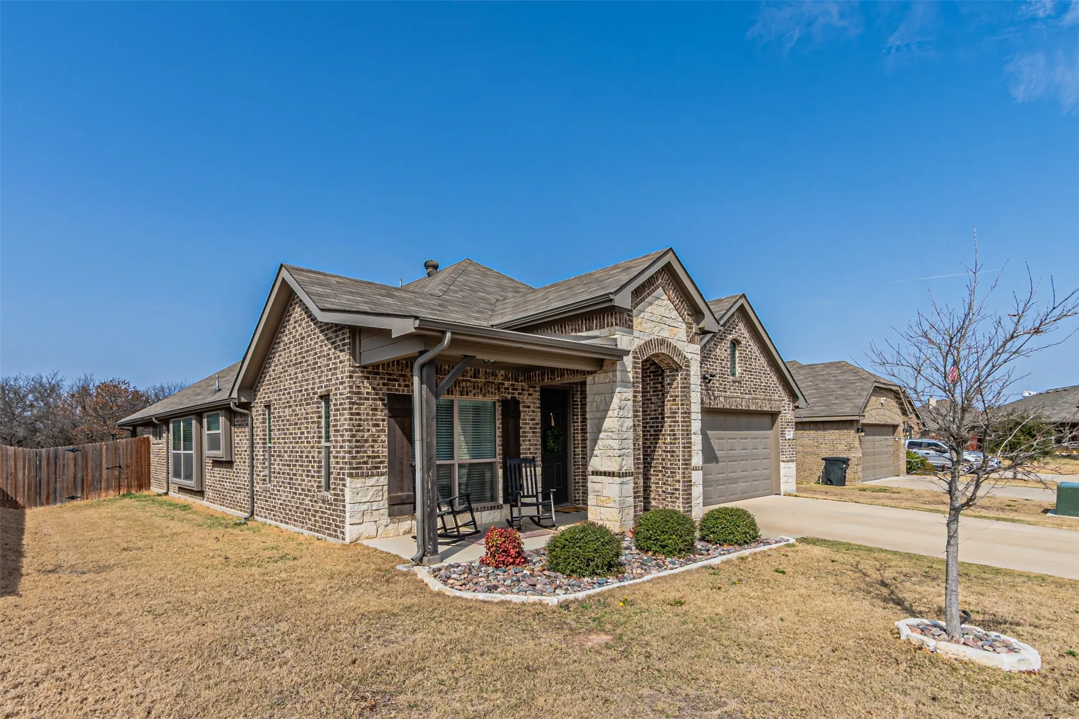 View of front of home with brick siding, concrete driveway, a garage, a porch, and stone siding