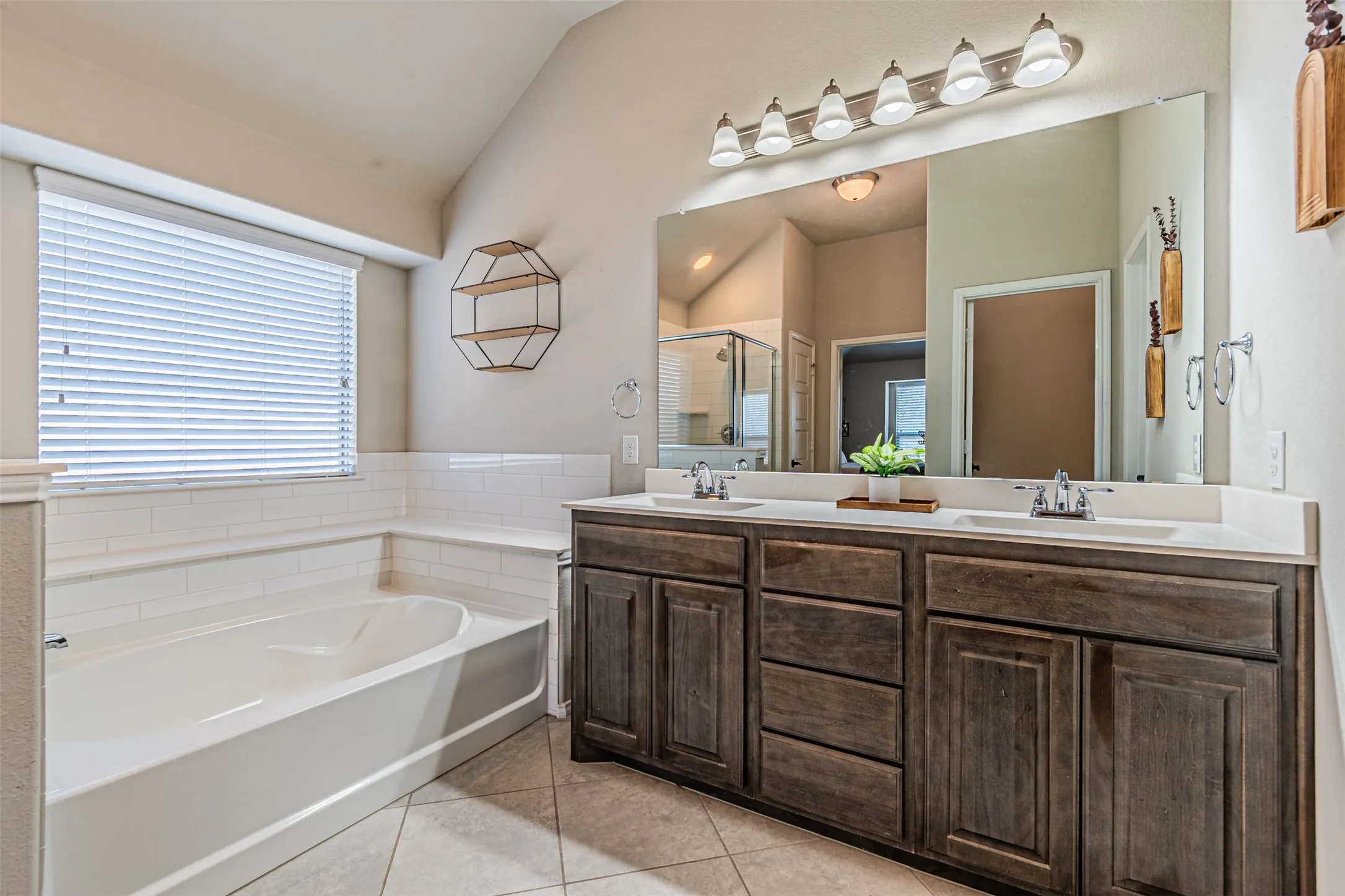 Bathroom with double vanity, a bath, light tile patterned flooring, lofted ceiling, and a shower stall