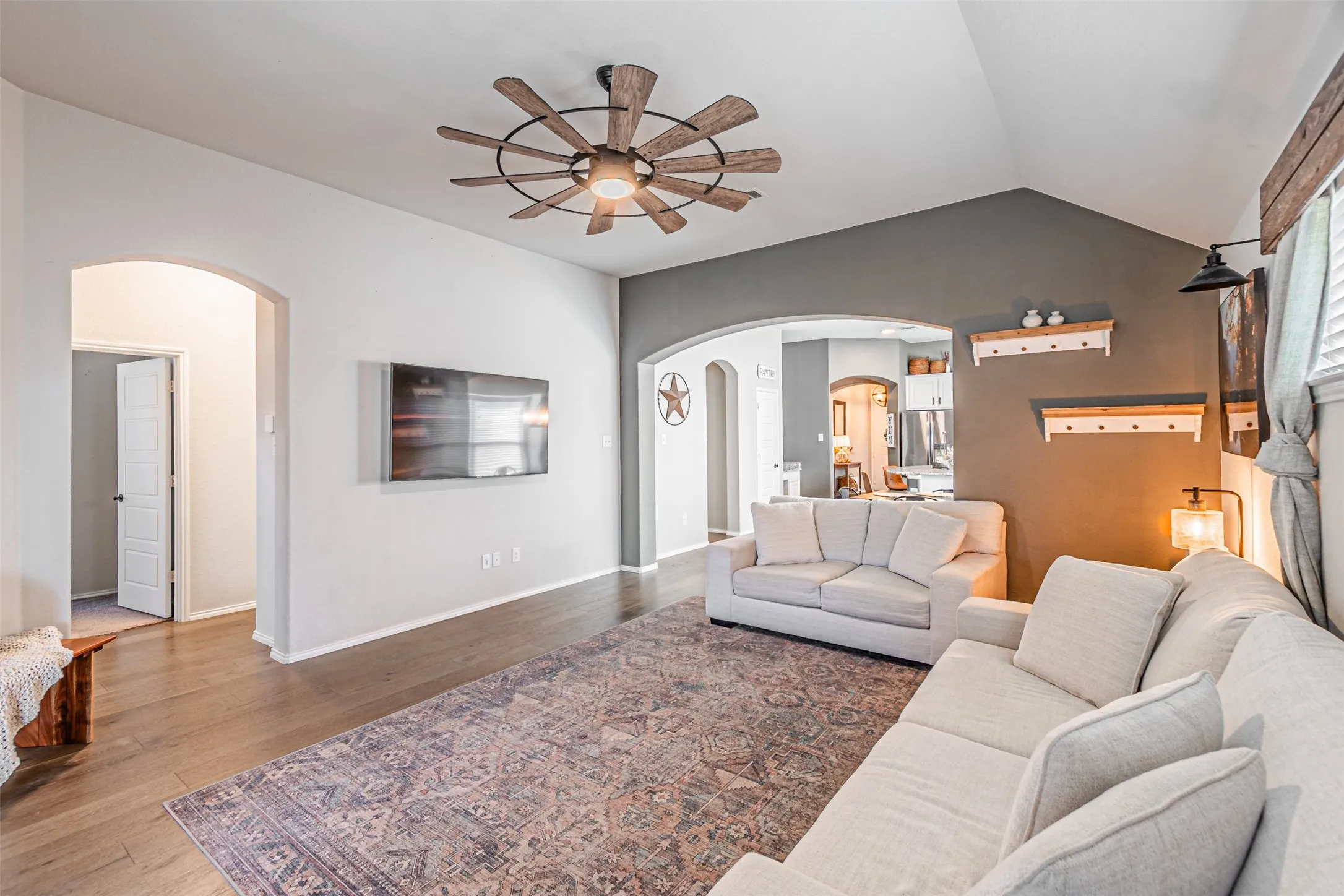 Living area featuring arched walkways, ceiling fan, vaulted ceiling, and wood finished floors