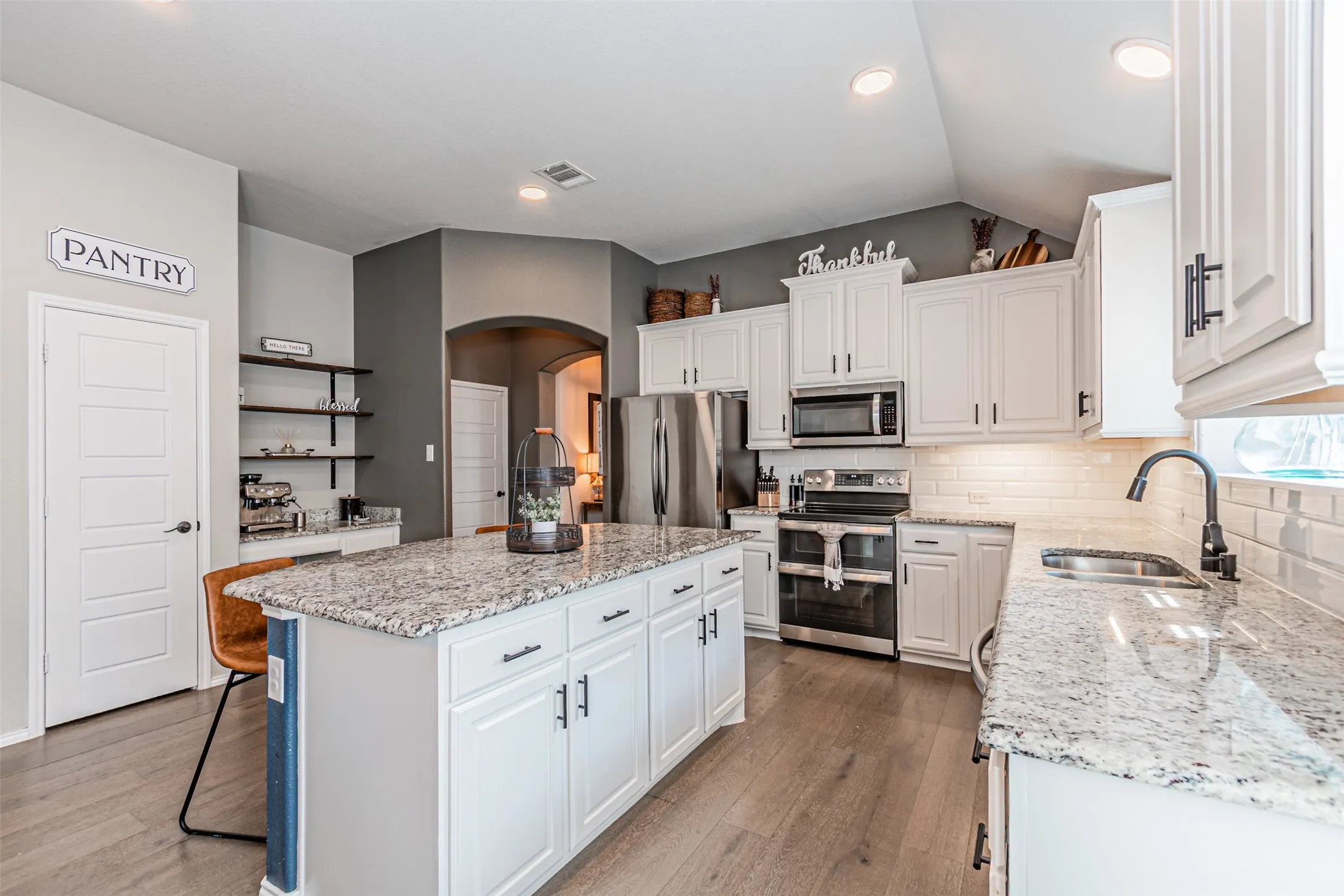 Kitchen featuring white cabinets, light stone counters, stainless steel appliances, light wood finished floors, and a kitchen island