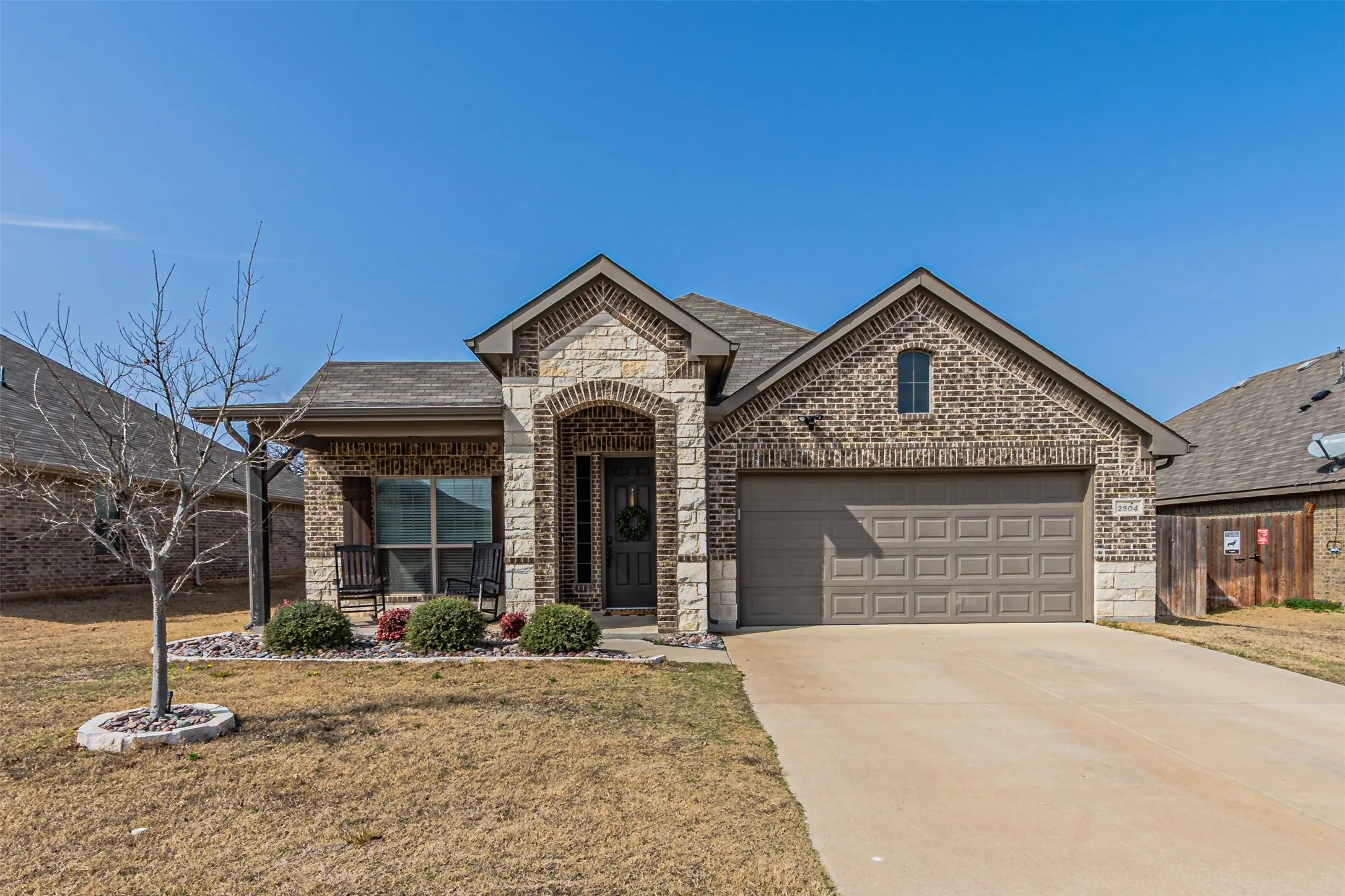 French country home with a front lawn, brick siding, concrete driveway, and stone siding