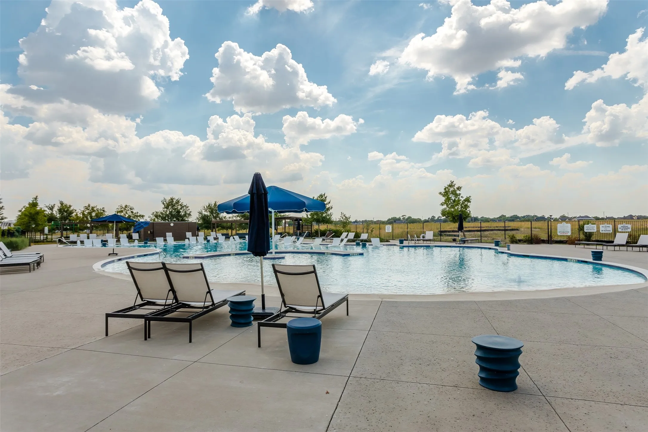 Curved swimming pool featuring a concrete surround, multiple lounge chairs, and blue shade umbrellas