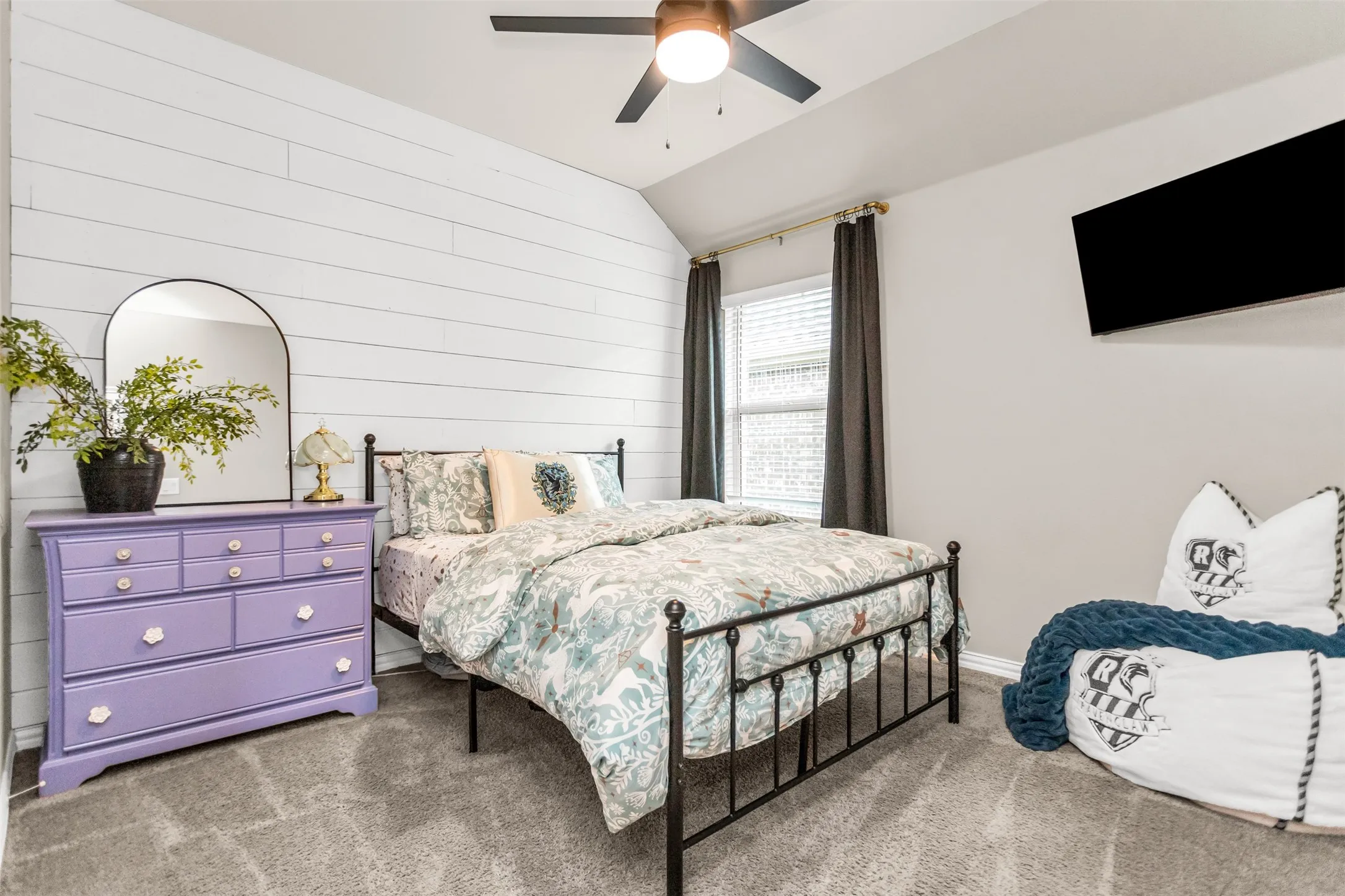 Carpeted room featuring a white shiplap accent wall, window with blinds, and a ceiling fan