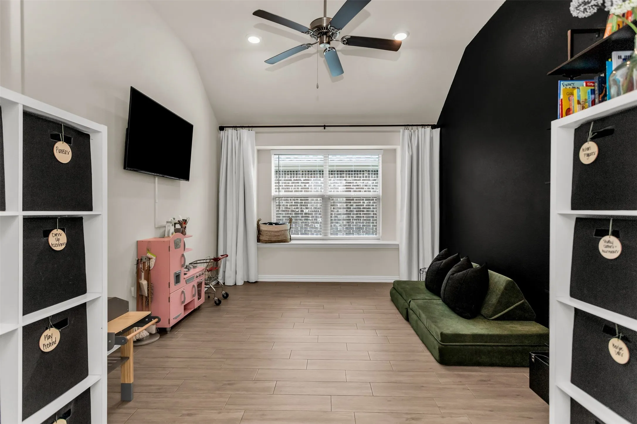 Vaulted ceiling with recessed lighting and ceiling fan, large window with window seat, wood-finish flooring, and a contrasting accent wall