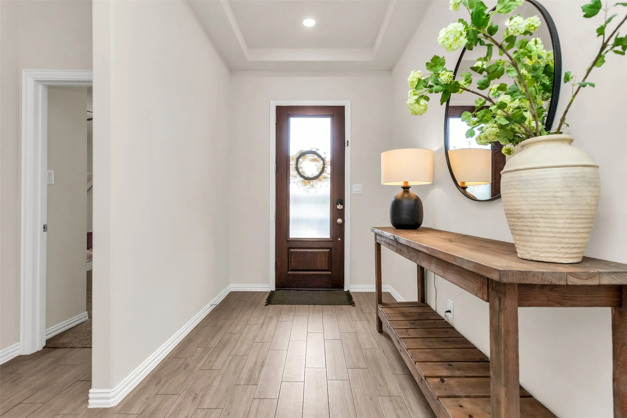 Recessed lighting, tray ceiling, wood-finish flooring, white trim, and a dark wood entry door with frosted glass