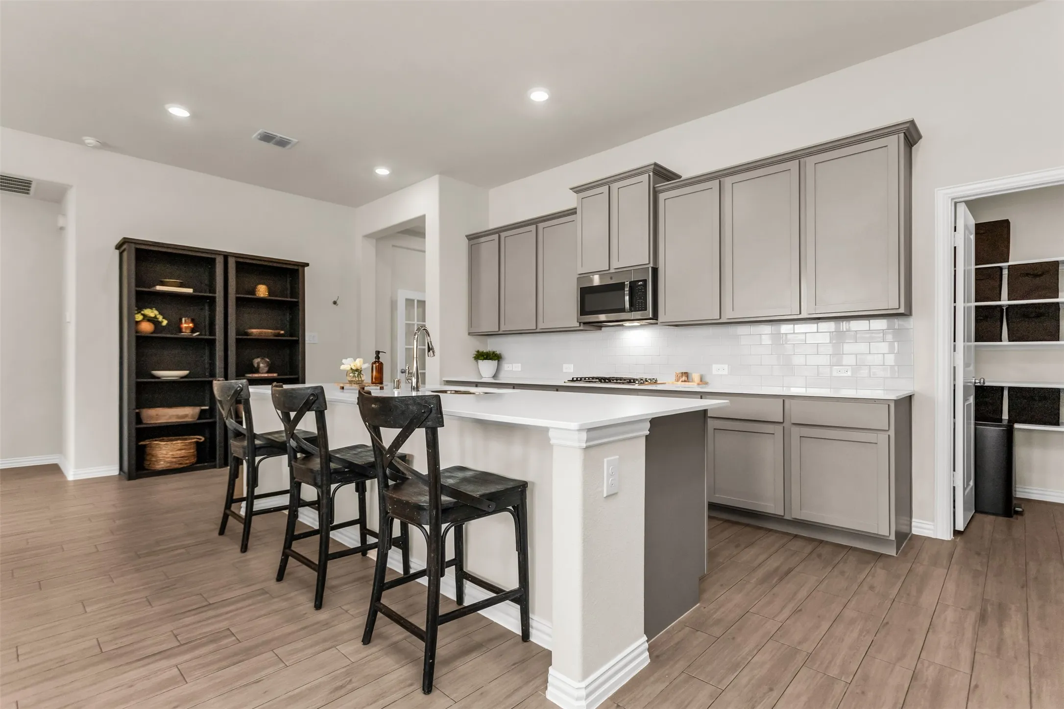 Well-appointed kitchen featuring light gray cabinetry, white subway tile backsplash, stainless steel appliances, a center island with seating, and wood-finish flooring