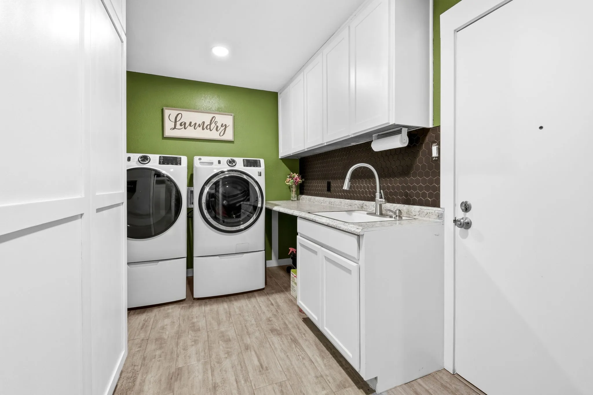 Wood-finish flooring, white cabinetry, a built-in sink with a gooseneck faucet, and a brown hexagonal tile backsplash