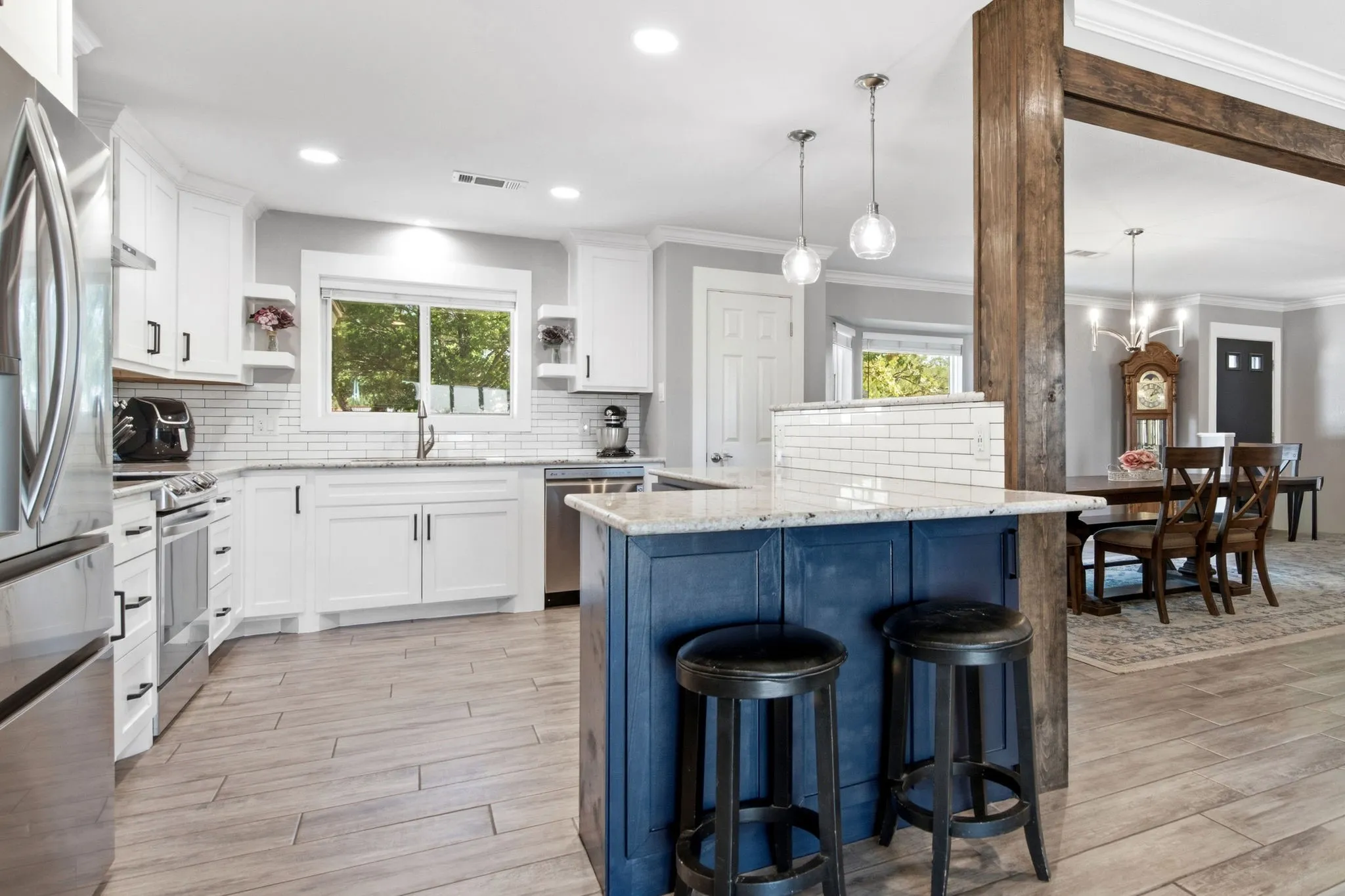 Gourmet kitchen with white cabinetry, stainless steel appliances, a white subway tile backsplash, and a blue island with pendant lighting