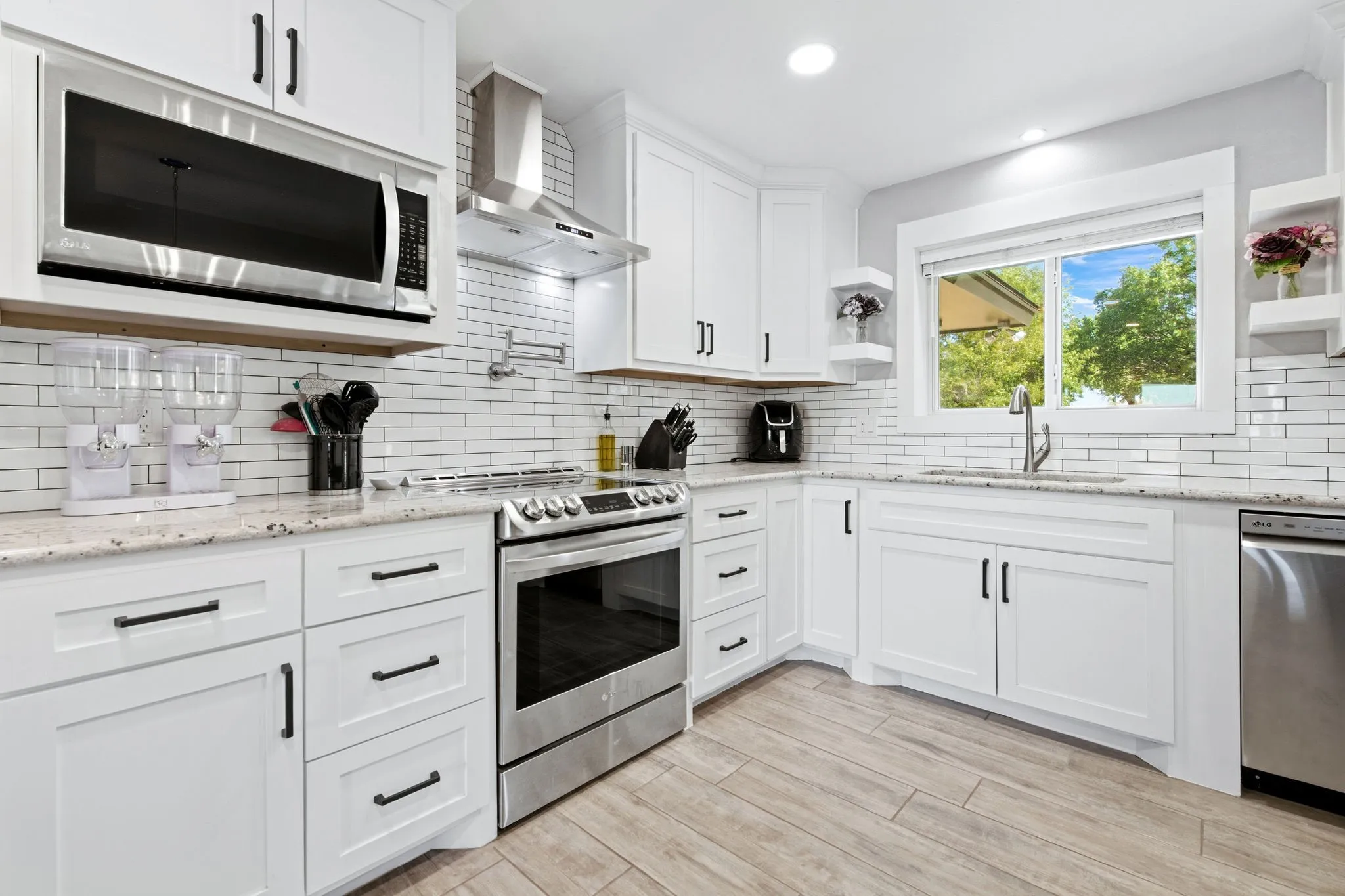 Kitchen with white shaker cabinetry, stainless steel appliances, speckled countertops, subway tile backsplash, and wood-finish flooring