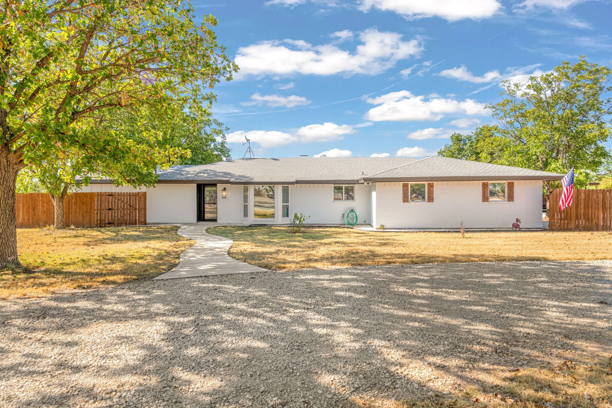 White exterior with a long gravel driveway, and a concrete pathway