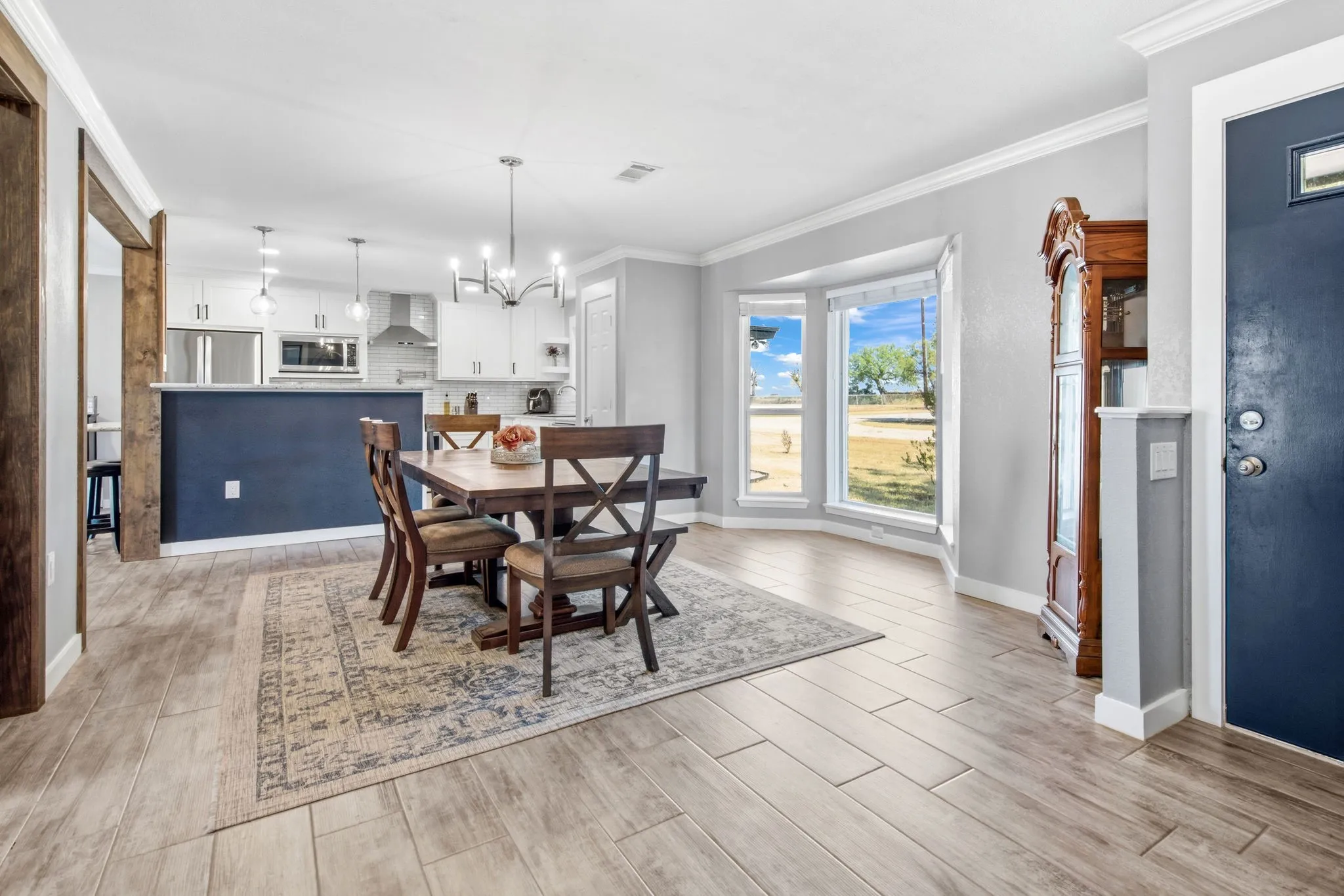 Open-concept living space featuring wood-finish flooring, a bay window, and a kitchen with white cabinetry and stainless steel appliances