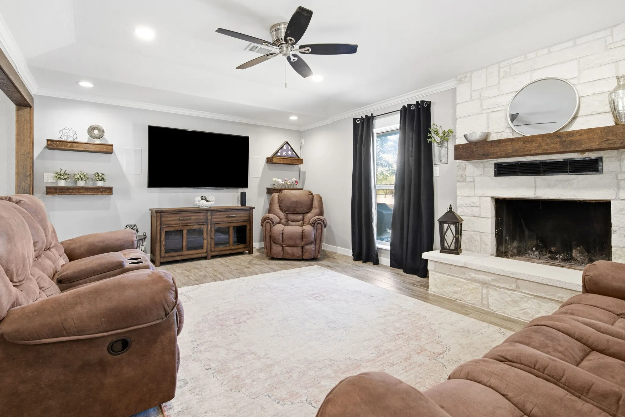 Living room with stone fireplace with wood mantel, wood-finish flooring, recessed lighting looking out to the private back yard