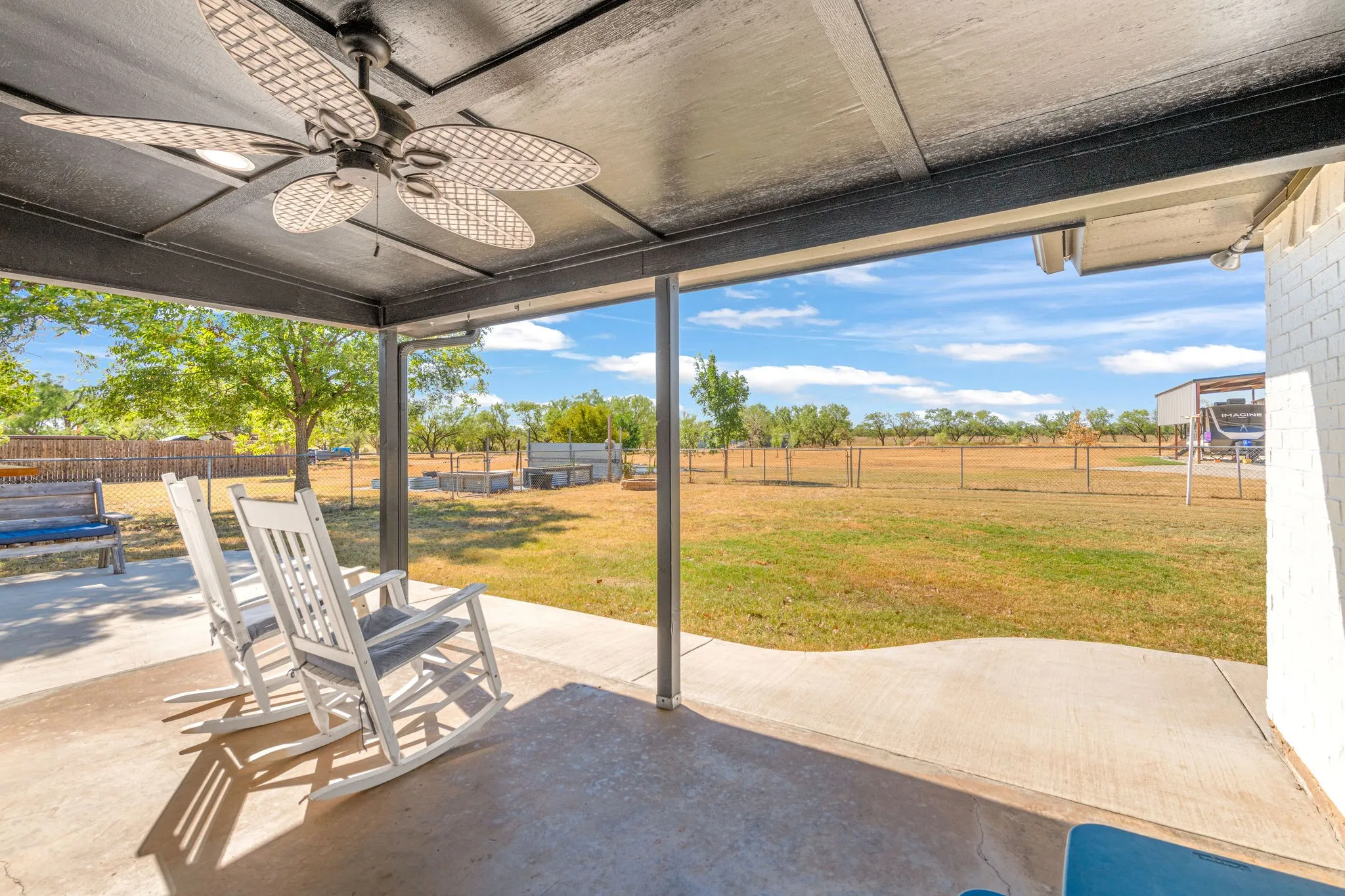 Covered patio with a ceiling fan, concrete flooring, and white brick siding