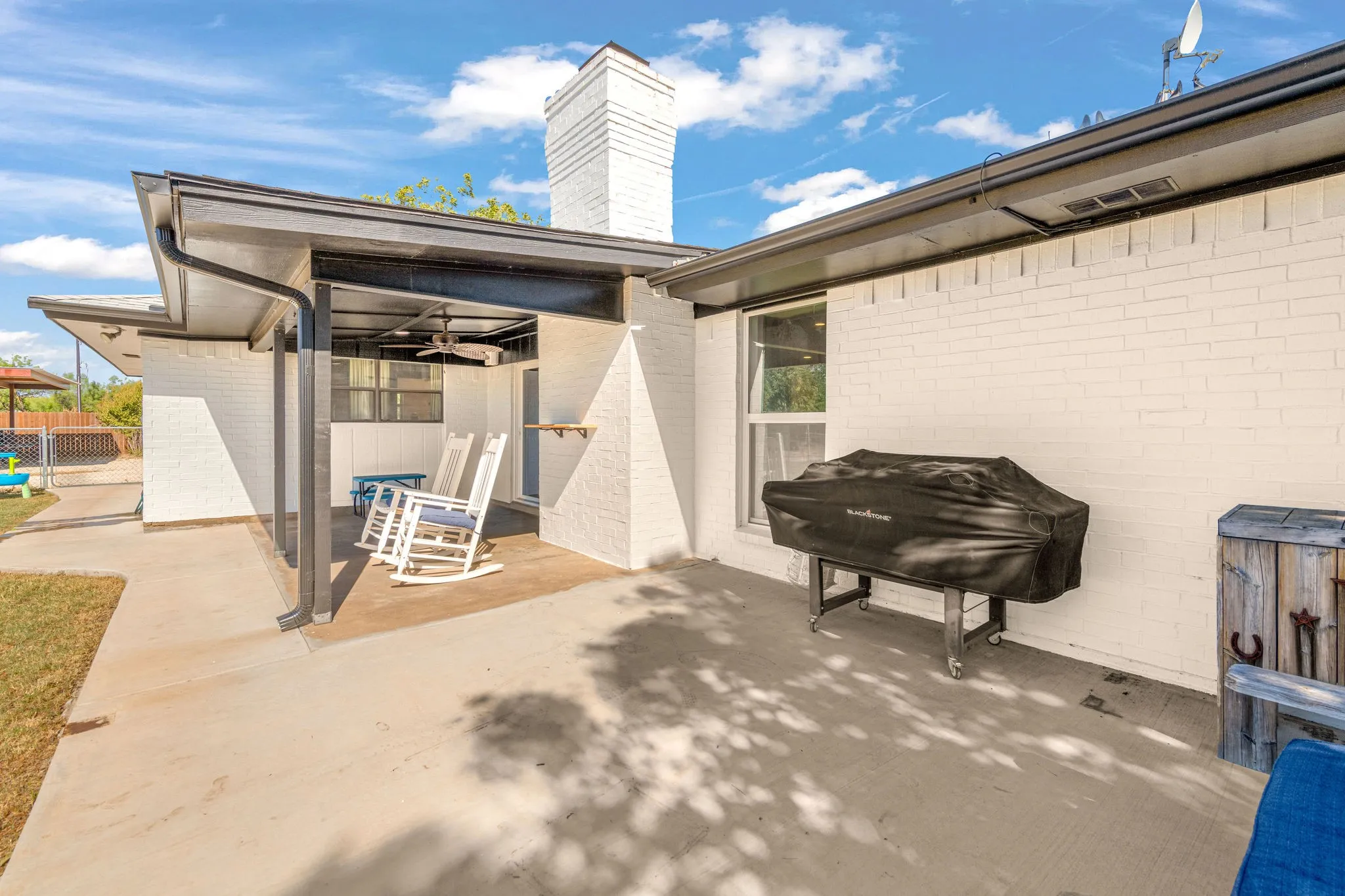 White brick exterior with a covered patio, featuring a ceiling fan and concrete flooring