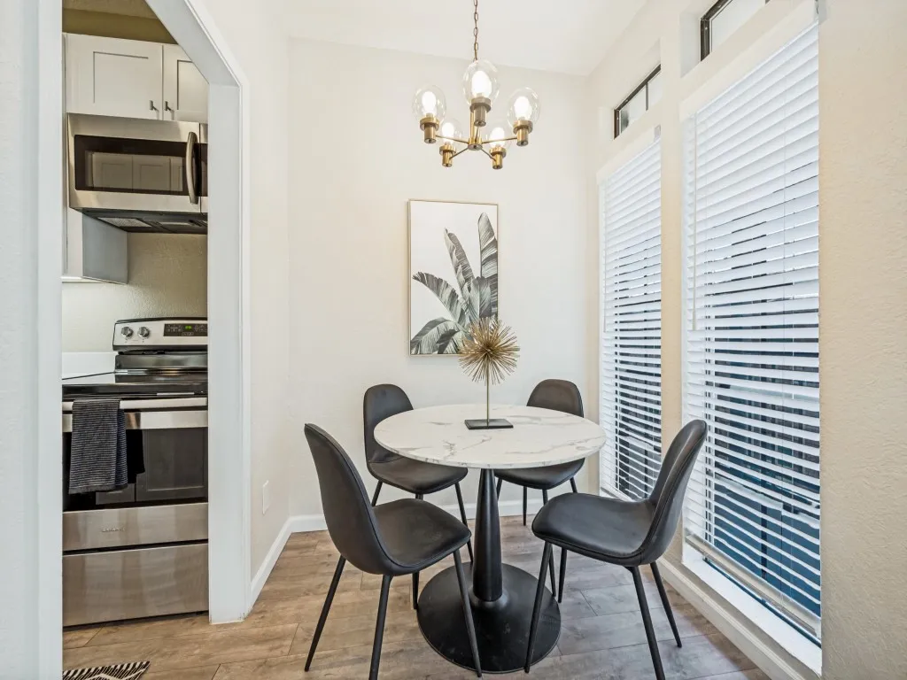 Dining area with wood-finish flooring, a contemporary chandelier, two large windows with blinds, and white walls