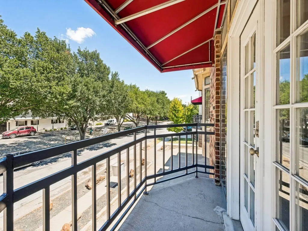 Balcony with a red fabric awning, black metal railing, and brick exterior