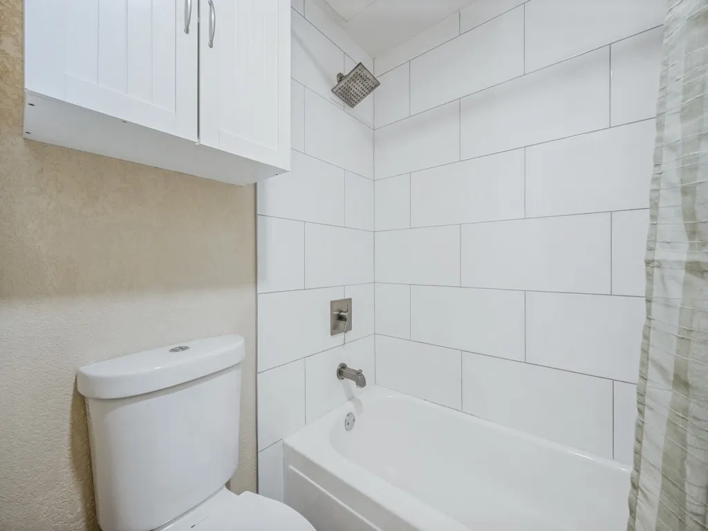 Bathroom featuring white subway tile shower surround, integrated bathtub, brushed nickel shower fixtures, and an overhead white shaker cabinet