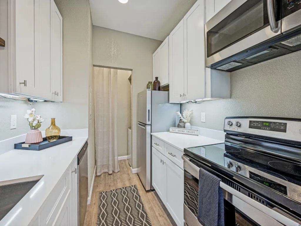 White cabinetry with brushed nickel hardware, stainless steel appliances, white countertops, wood-finish flooring, and recessed lighting