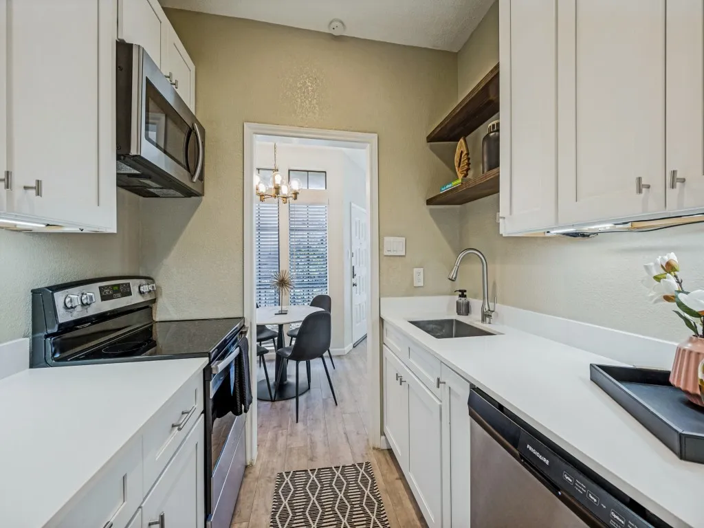 White cabinetry with brushed nickel hardware, stainless steel appliances, pristine white countertops, wood-finish flooring, and open shelving