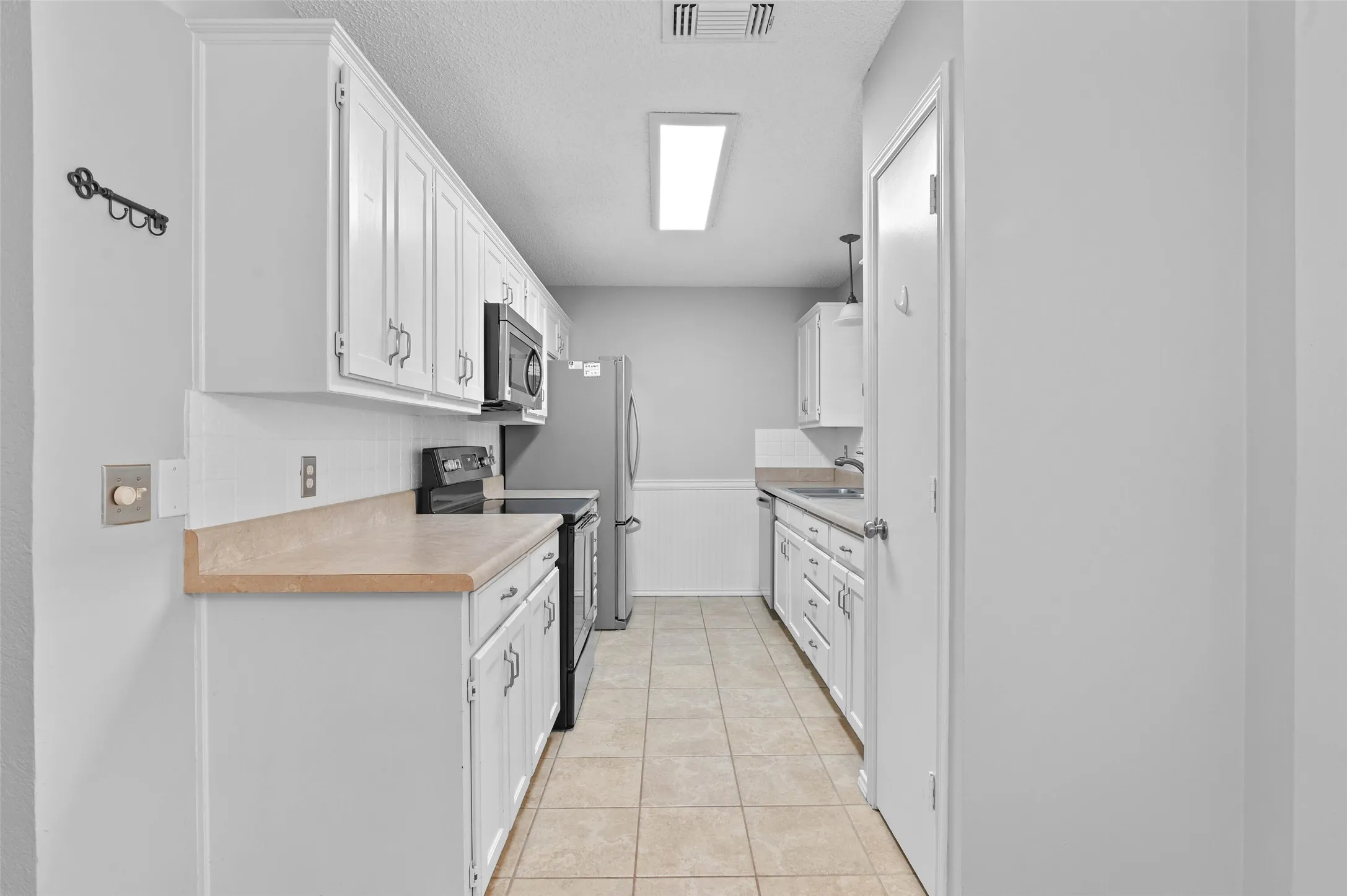 Galley kitchen with pantry, electric range, microwave and refrigerator.