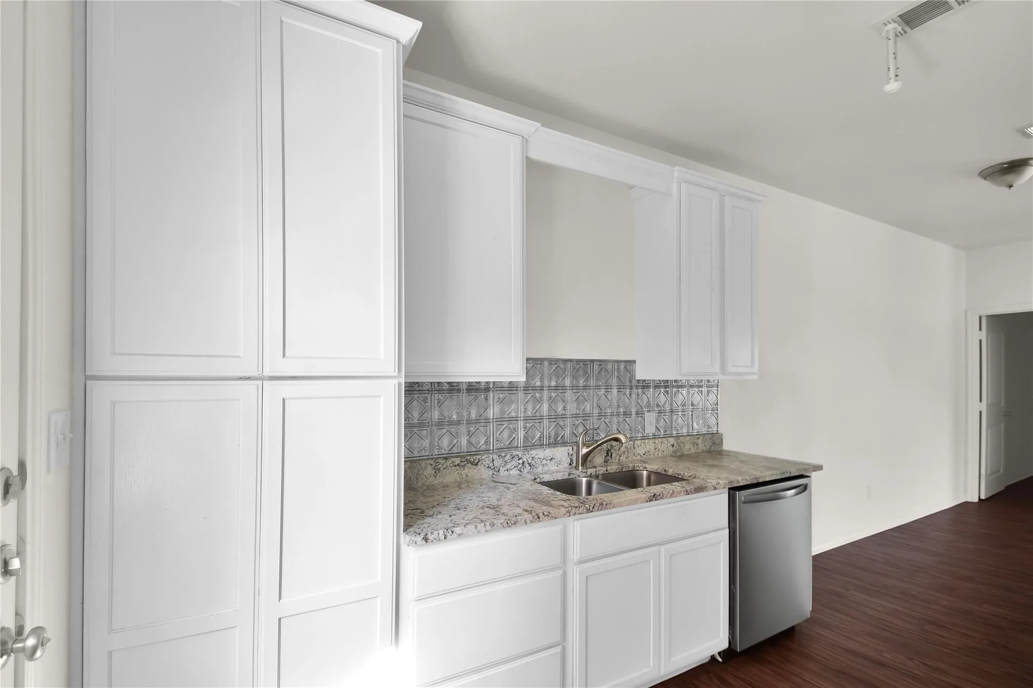White shaker cabinetry, stainless steel dishwasher, dual basin sink, patterned tile backsplash, and stone-finish countertop