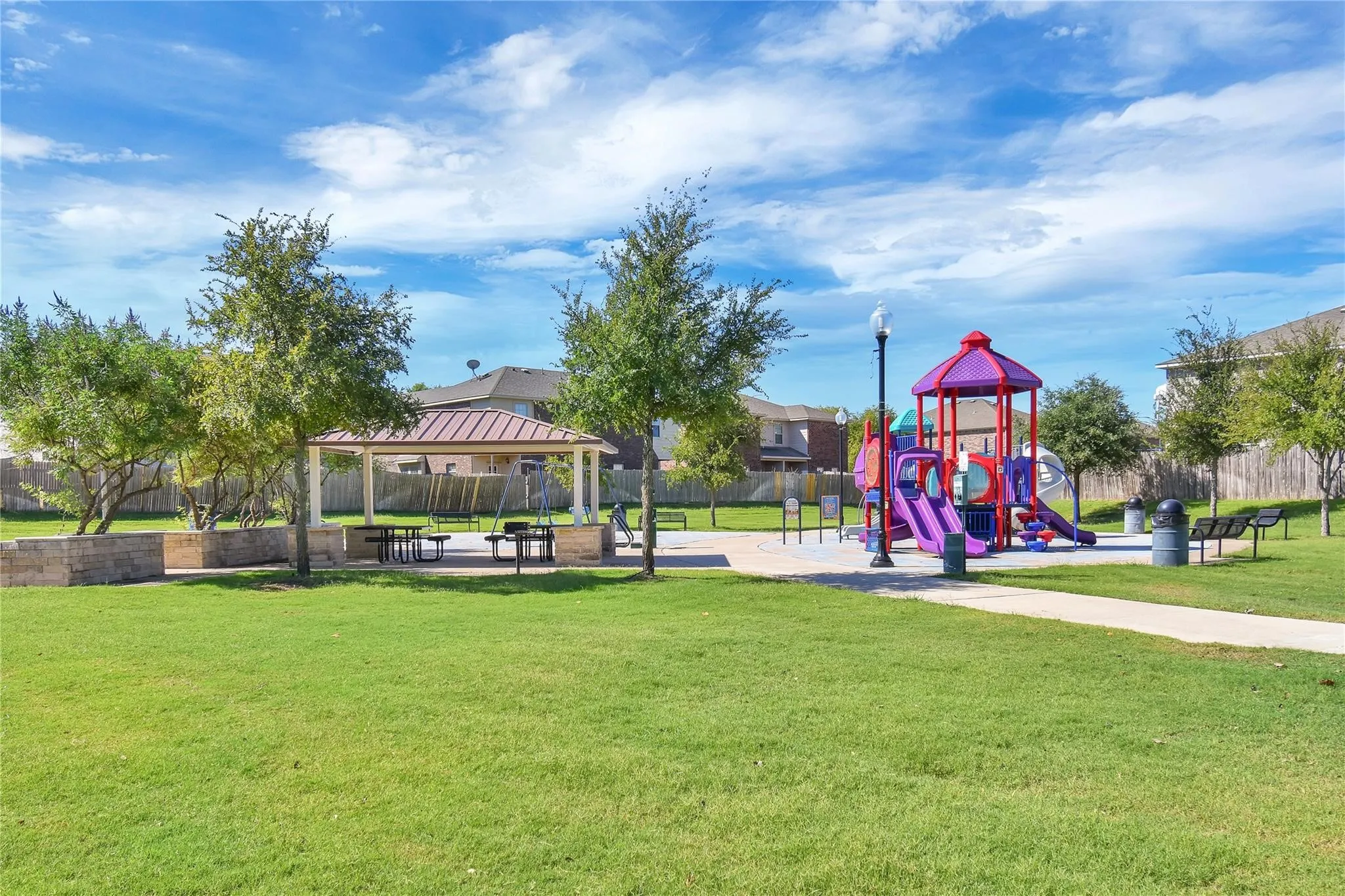 Community playground featuring multiple slides and climbing elements, a covered picnic area with seating, and a paved pathway