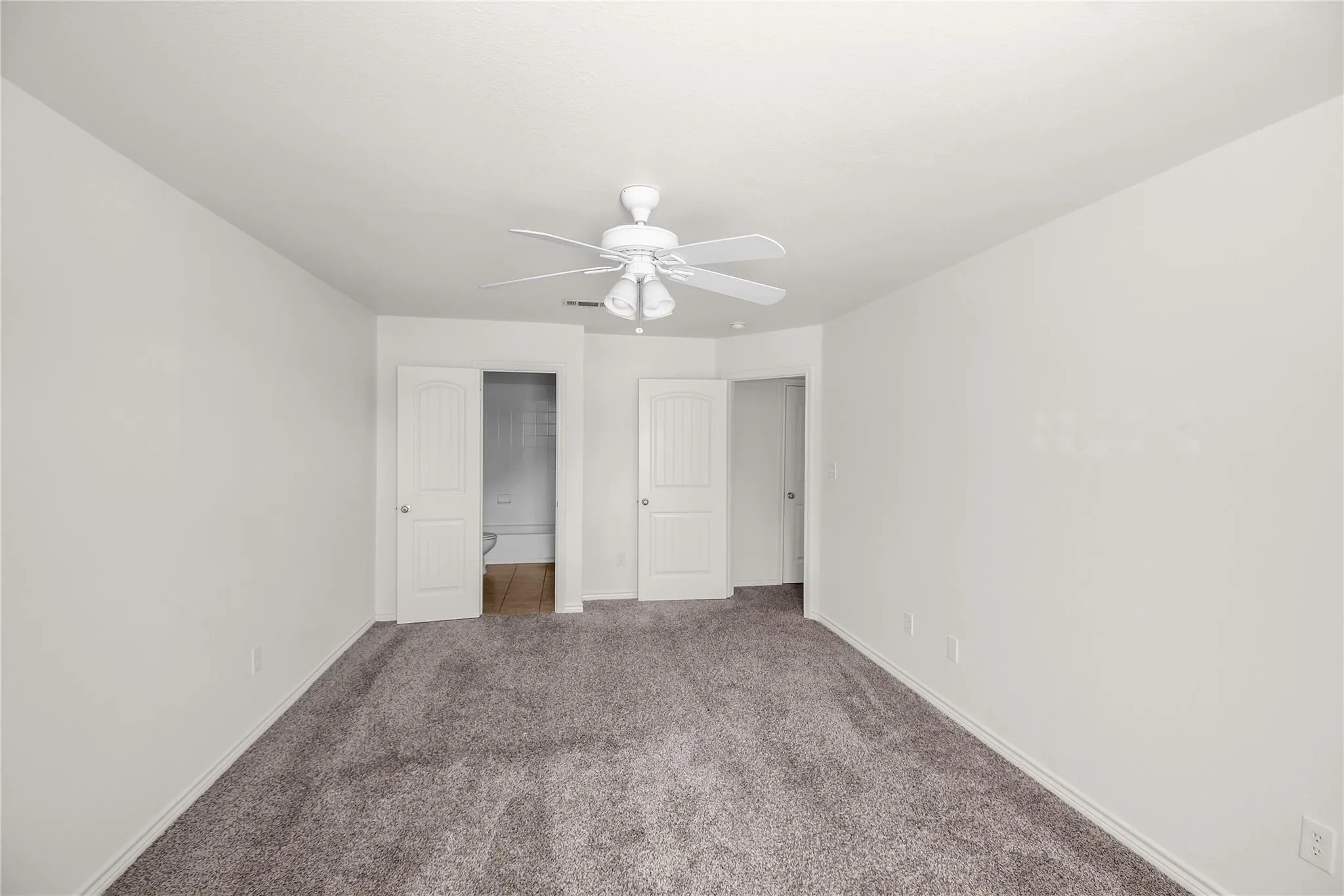 Spacious room featuring neutral carpeting, a ceiling fan with light fixture, and two panel doors